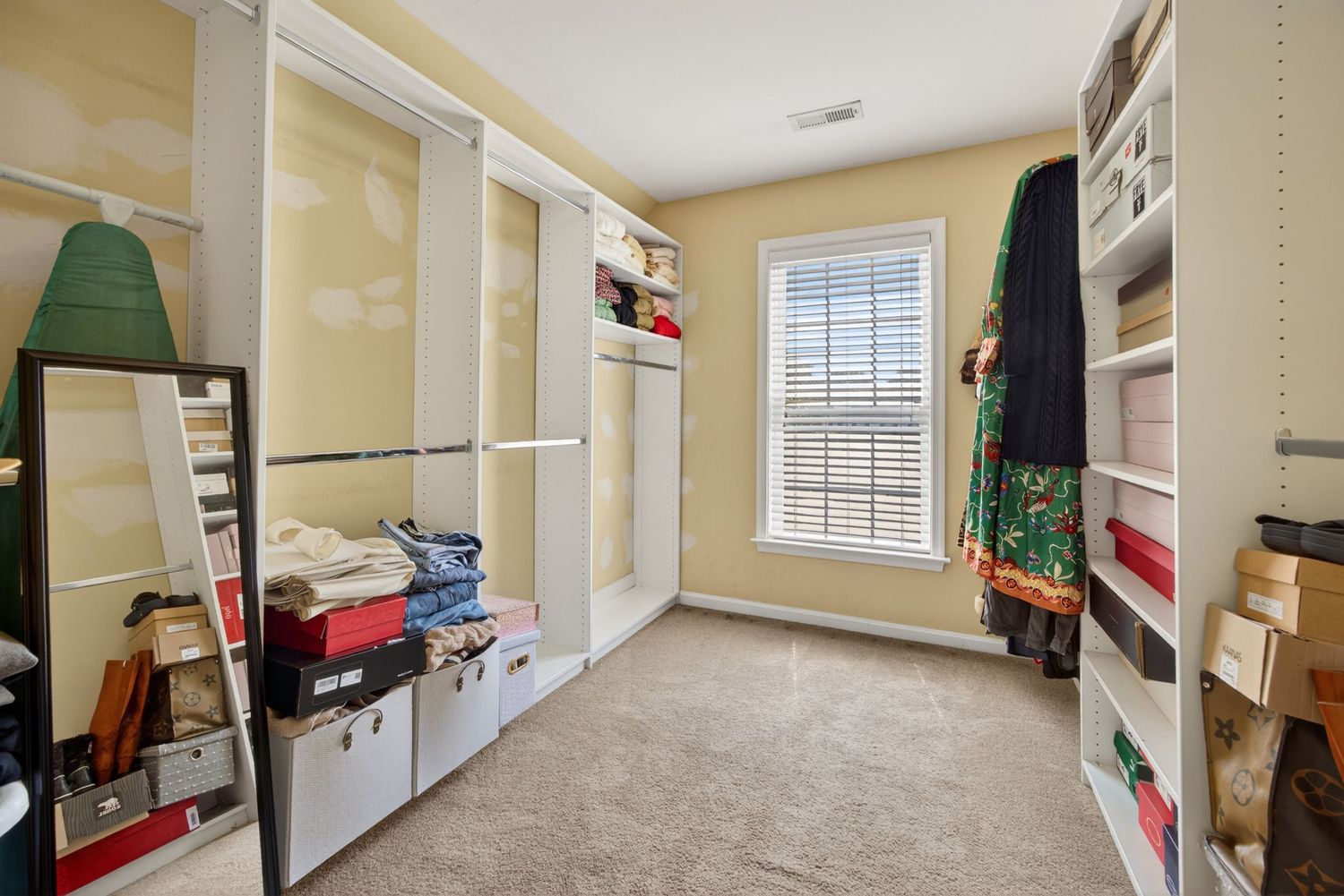 Spacious walk-in closet with built-in shelving, mirrored sliding doors, and a window providing natural light.
