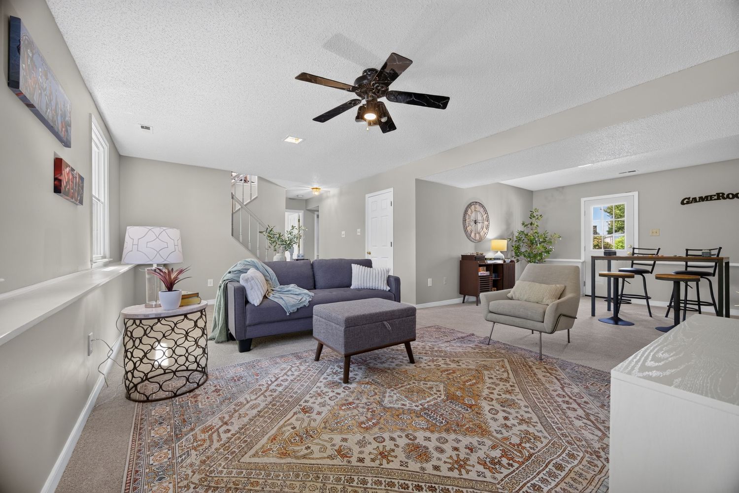 Spacious living room with gray sofa, ceiling fan, patterned area rug, and dining area in background.