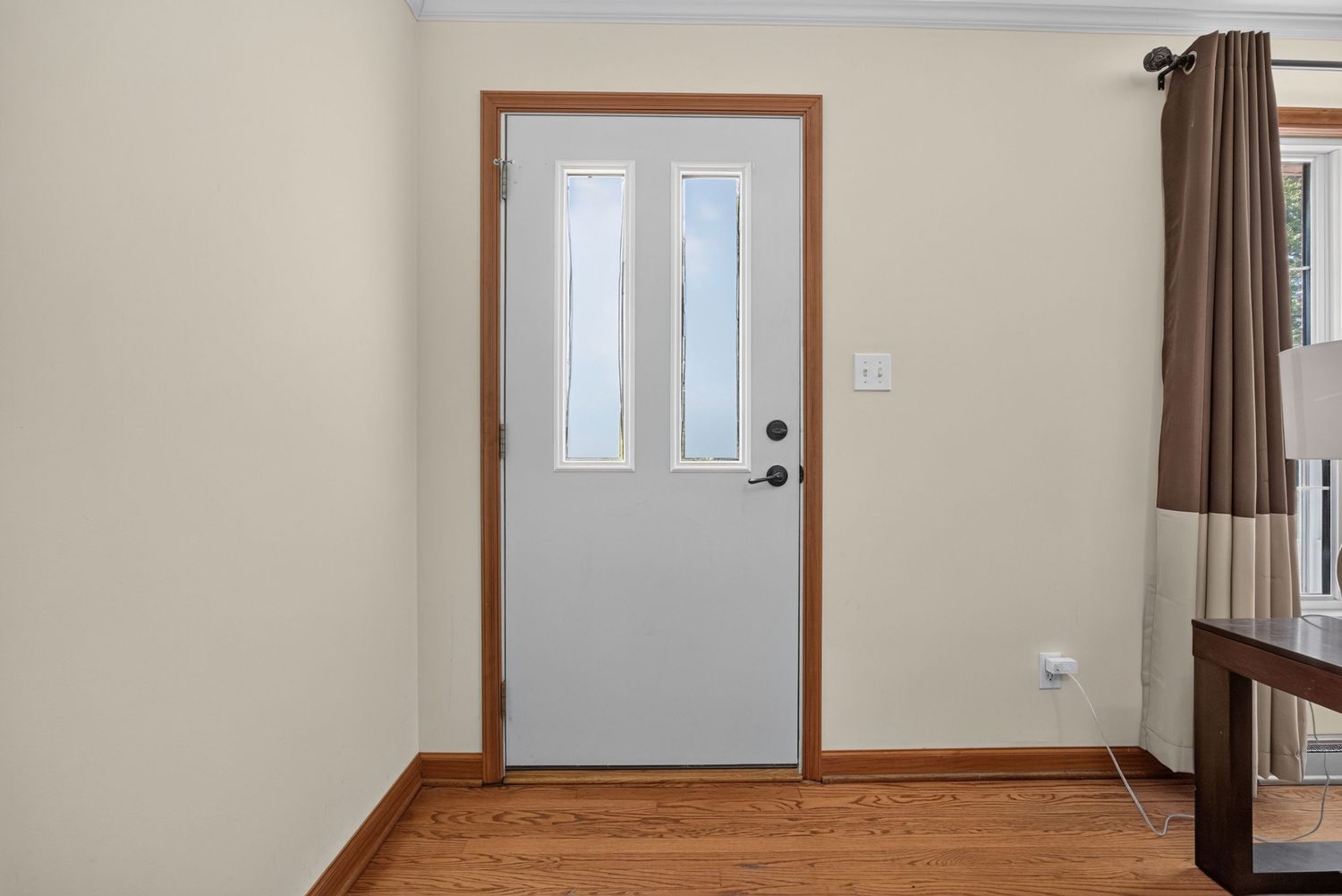 White interior door with glass panels, wood trim, and hardwood floors in a bright, neutral-toned room.