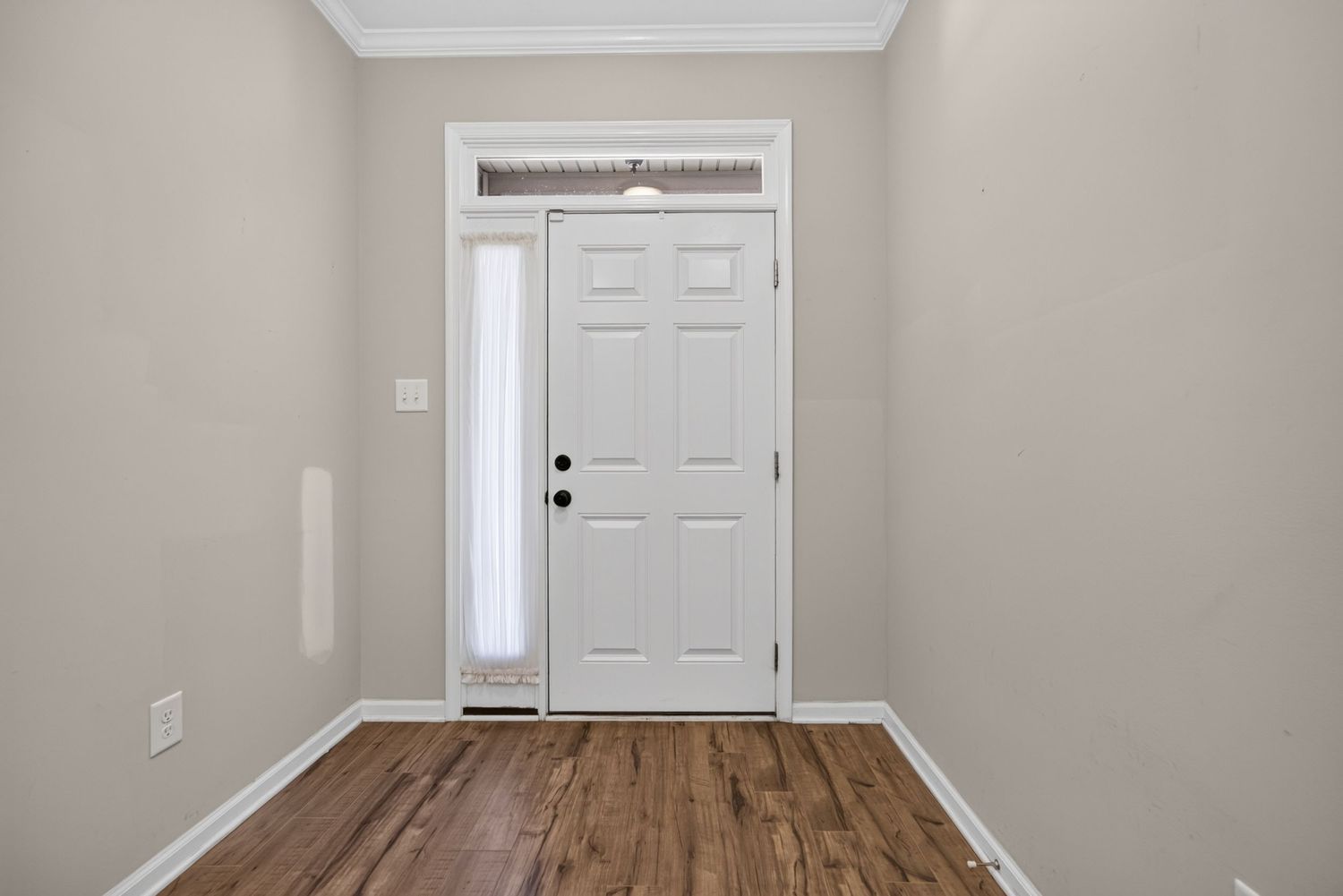 Bright entryway with white six-panel door, transom window, sidelight, crown molding, and dark hardwood floors.