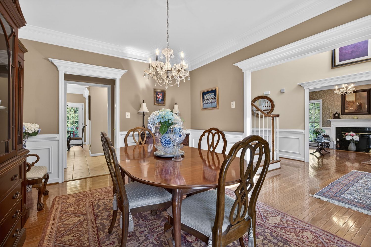 Elegant dining room with oval wood table, chandelier, crown molding, hardwood floors, and Persian rug in a classic colonial home.