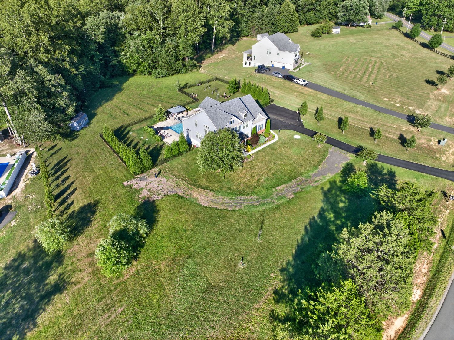 Aerial view of a suburban home with lush green lawn, landscaped hedges, pool, and winding driveway surrounded by trees.