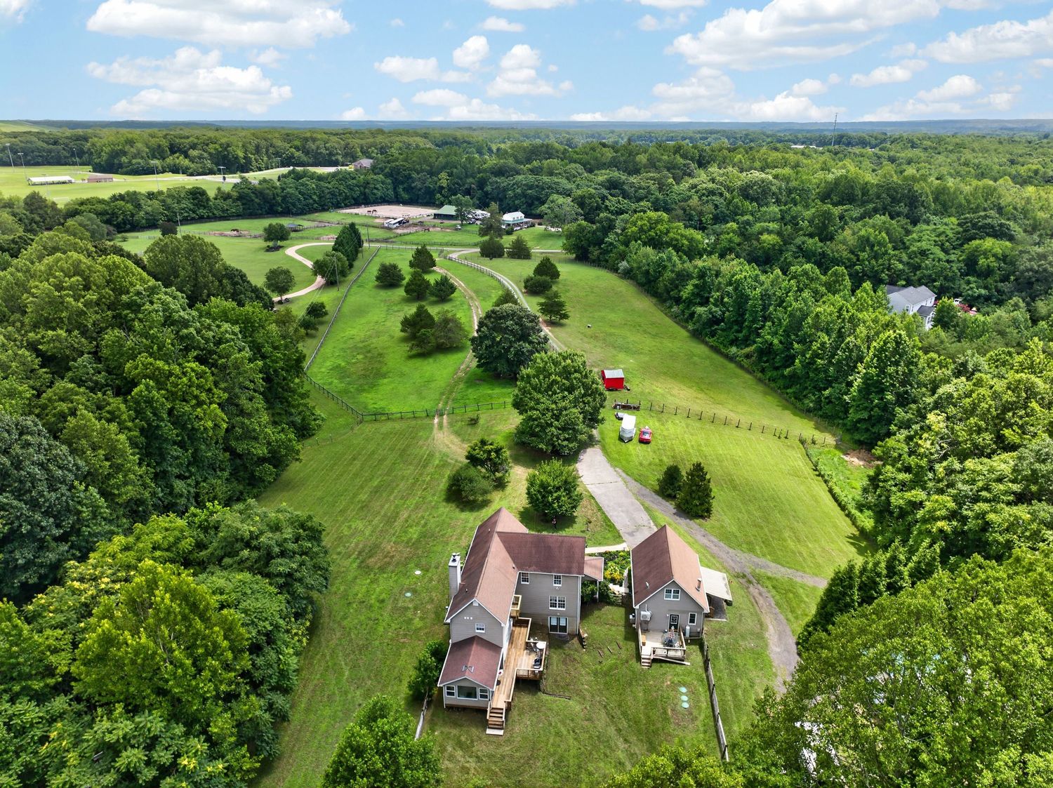 Aerial view of a rural property with a house surrounded by lush green trees and open fields in a countryside setting.