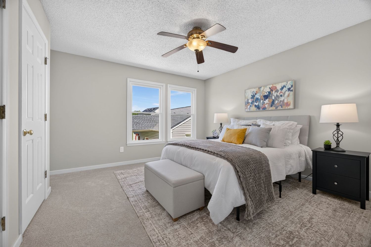 Bright bedroom with ceiling fan, gray carpet, upholstered bed, dark nightstands, and a window with scenic views.