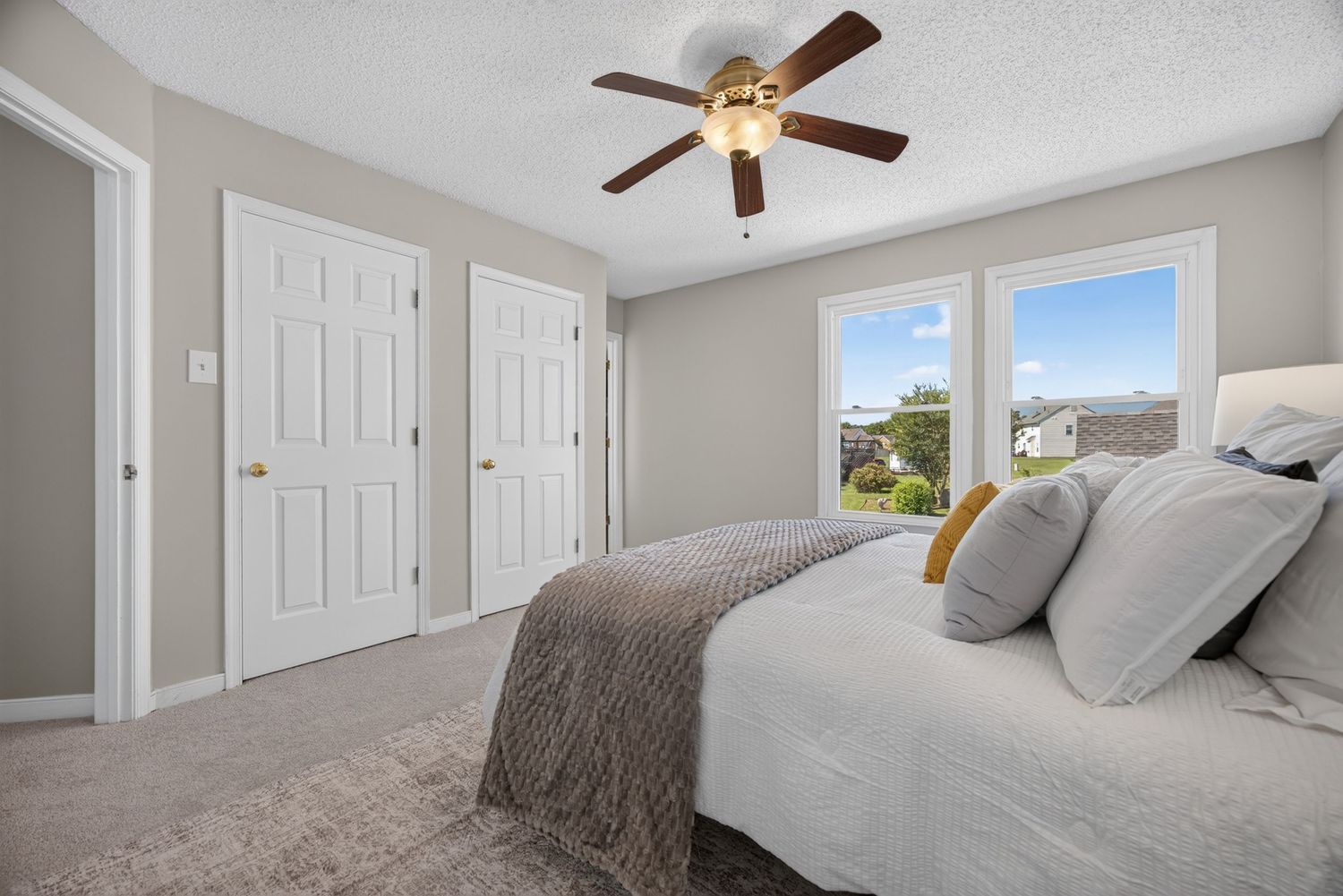 Spacious bedroom with ceiling fan, plush carpet, large window, and two white doors leading to closet and hallway.