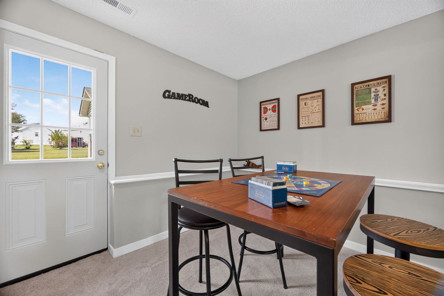 Game room with wooden dining table, bar stools, framed wall art, and a door leading outside with natural light.