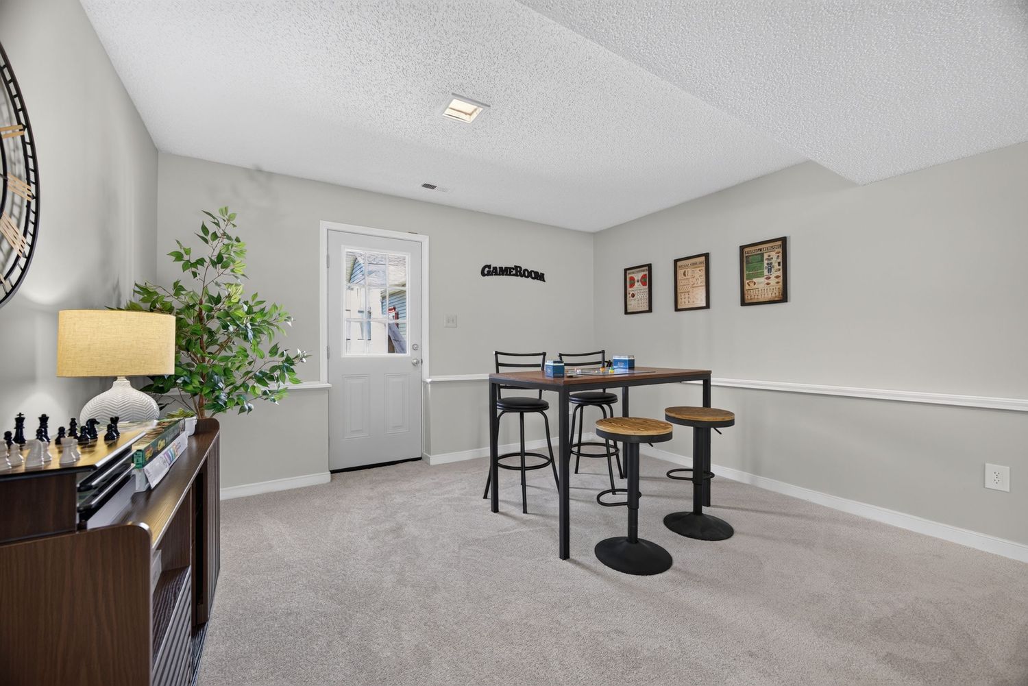 Cozy basement game room with carpet, bar-height table, stools, and a decorative plant near a white door.