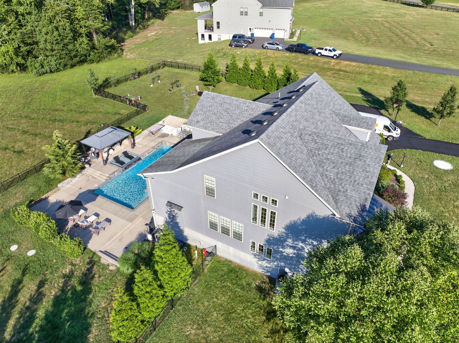 Aerial view of a large suburban home with a backyard pool, patio, and lush green lawn on a sunny day.