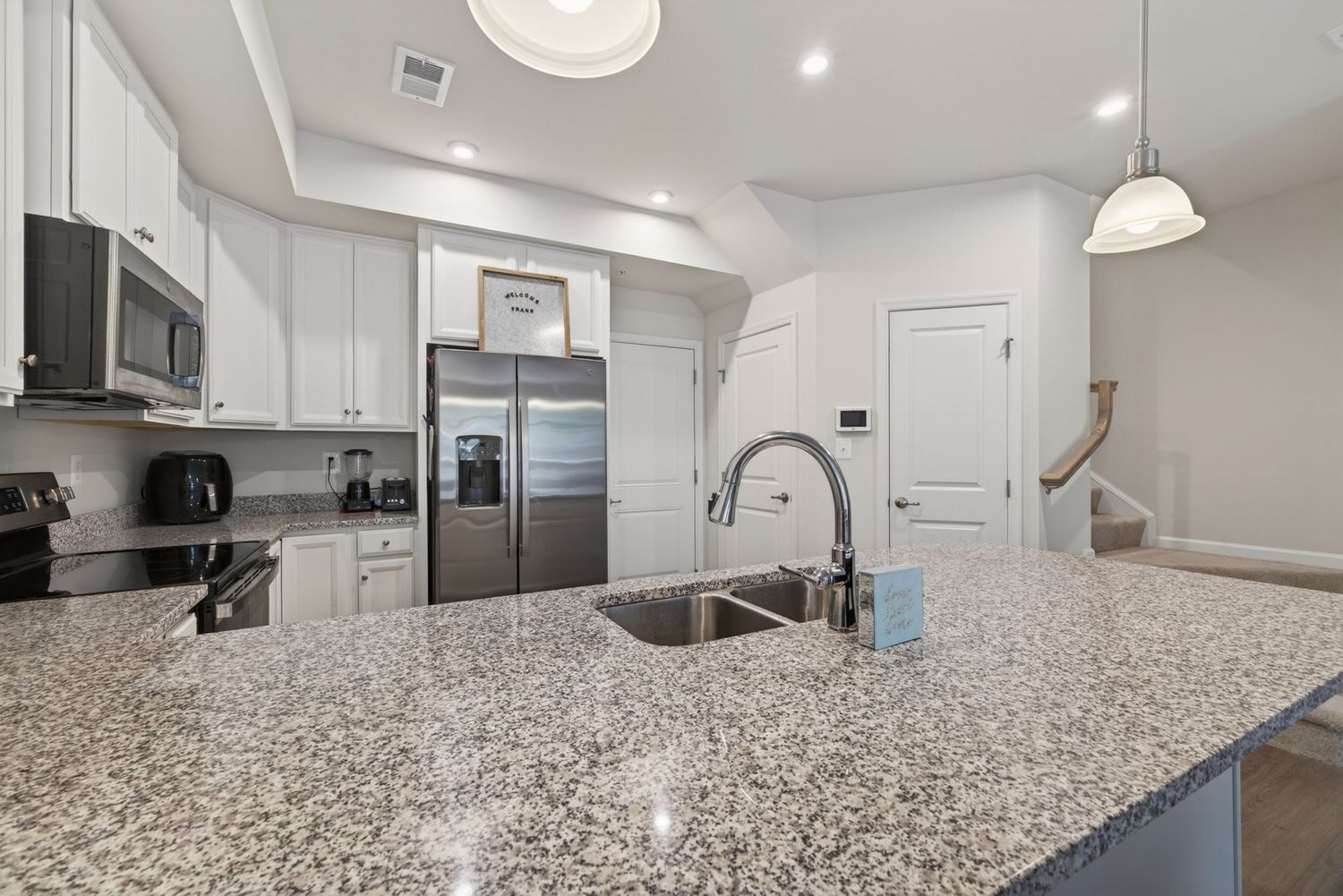Modern kitchen with granite island, stainless steel appliances, white cabinets, and pendant lighting.
