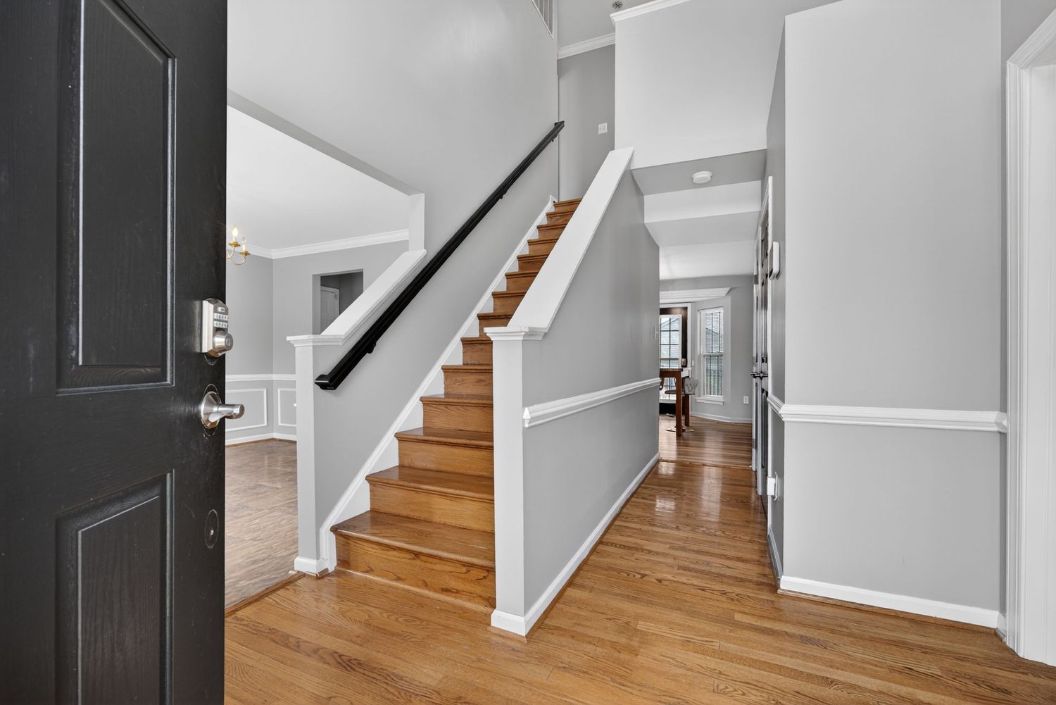 Bright entryway with hardwood floors, white staircase with dark handrail, and open hallway leading to living spaces.
