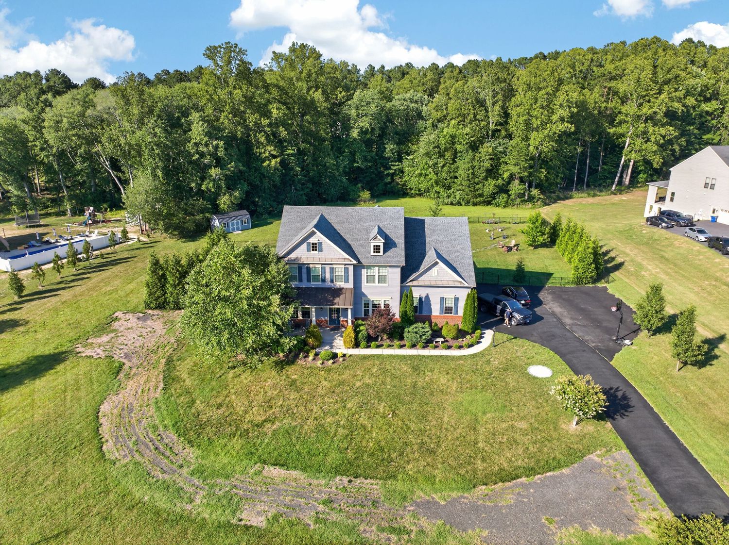 Aerial view of a large two-story home surrounded by lush green trees and manicured lawn with paved driveway.