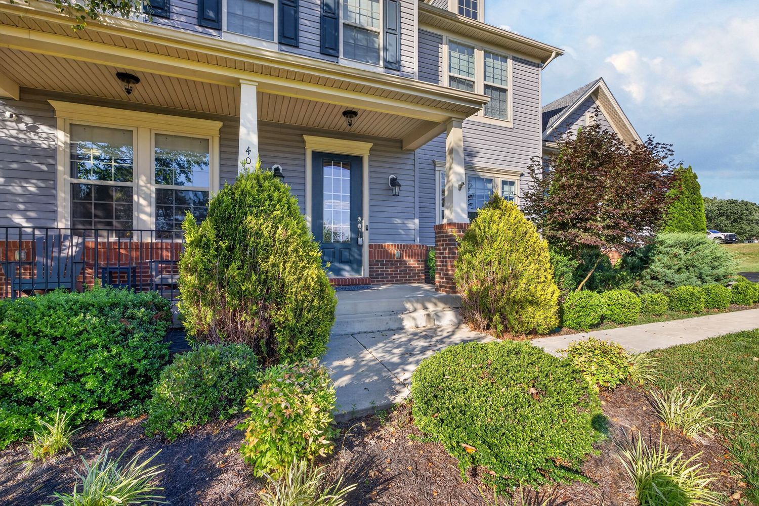 Charming suburban home entrance with manicured shrubs, mulched landscaping, covered porch, and a welcoming stone pathway.