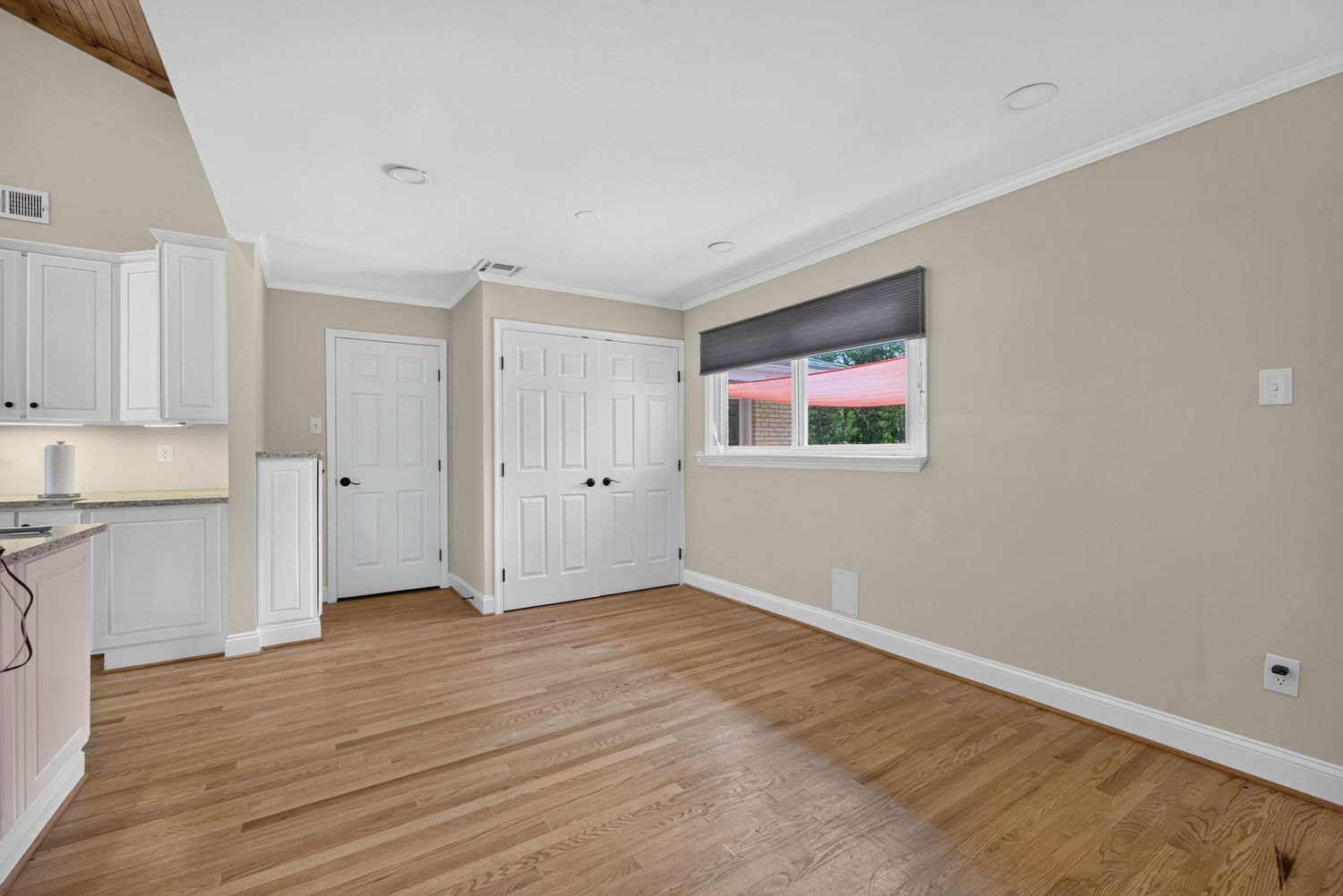 Bright empty room with hardwood floors, white trim, crown molding, closet doors, and a window with natural light.