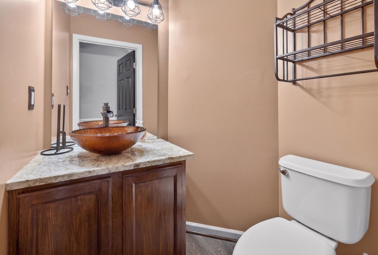 Small bathroom with dark wood vanity, copper vessel sink, marble countertop, white toilet, and wall-mounted metal shelf.