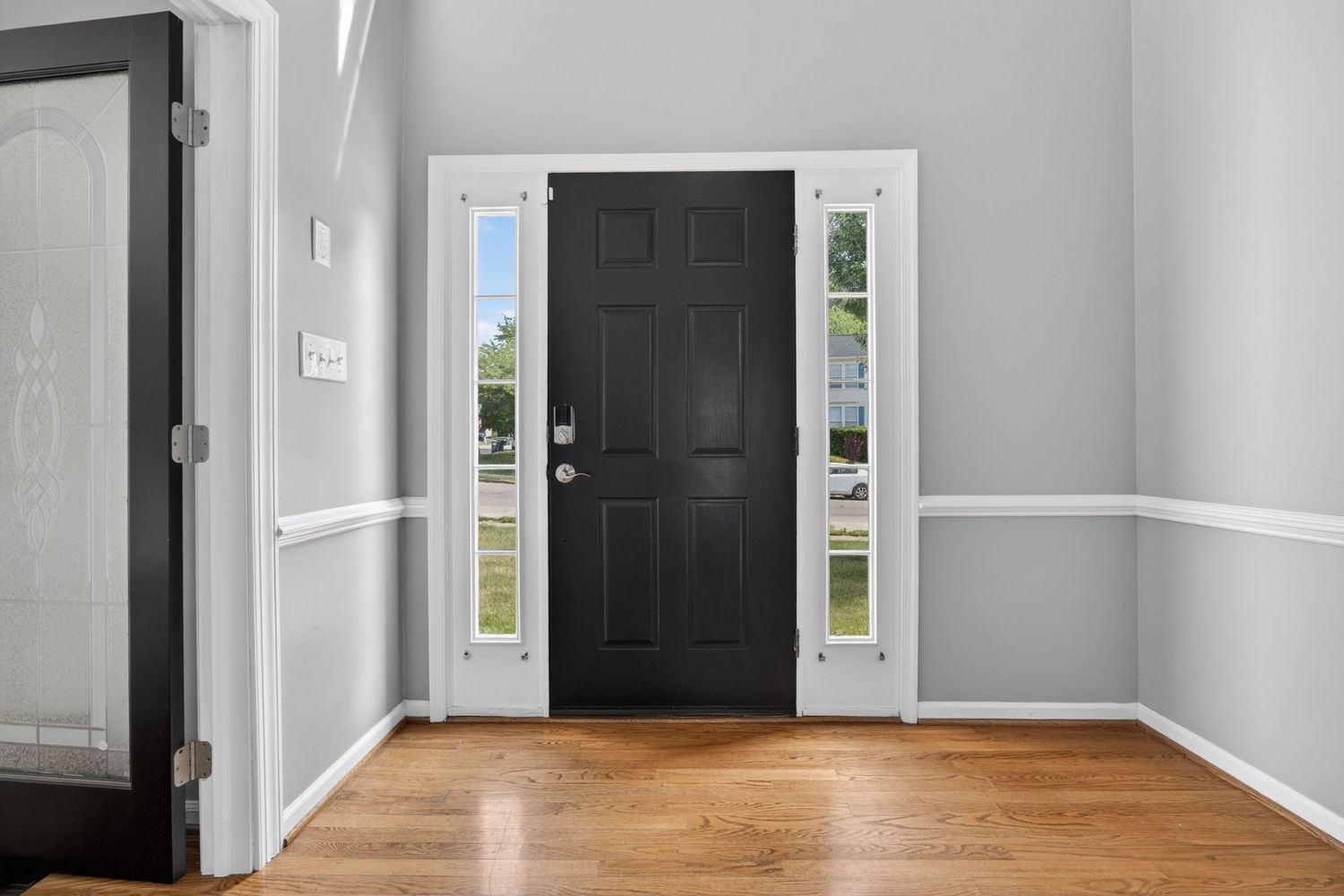 Bright entryway with black front door, sidelights, white wainscoting, and hardwood floors in a modern home.