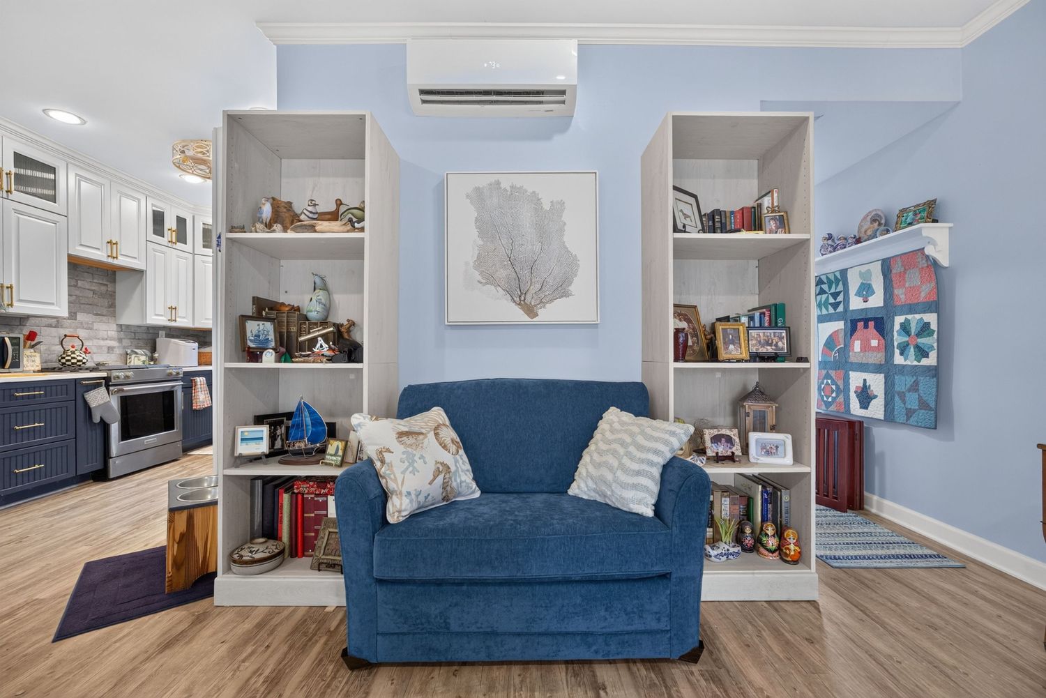 Cozy living area with blue sofa, built-in white shelves, hardwood floors, and mini-split AC unit on light blue walls.
