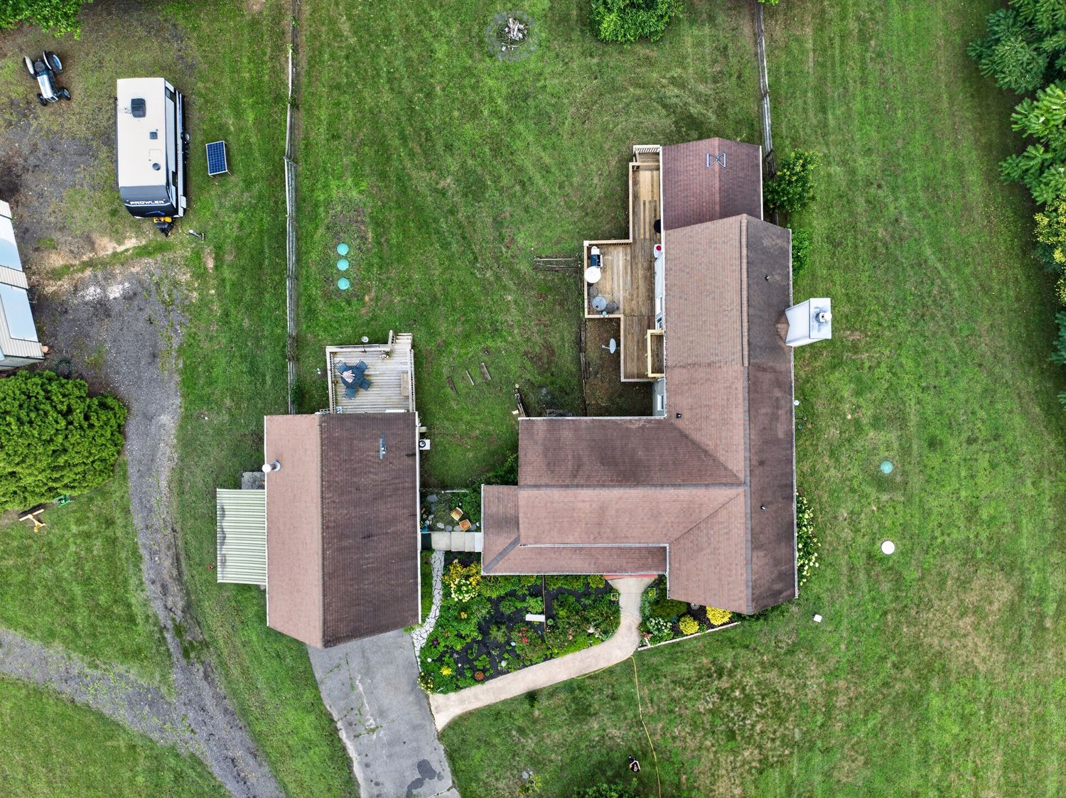 Aerial drone view of two brown-roofed homes surrounded by lush green lawn with trees and a white RV in rural setting.