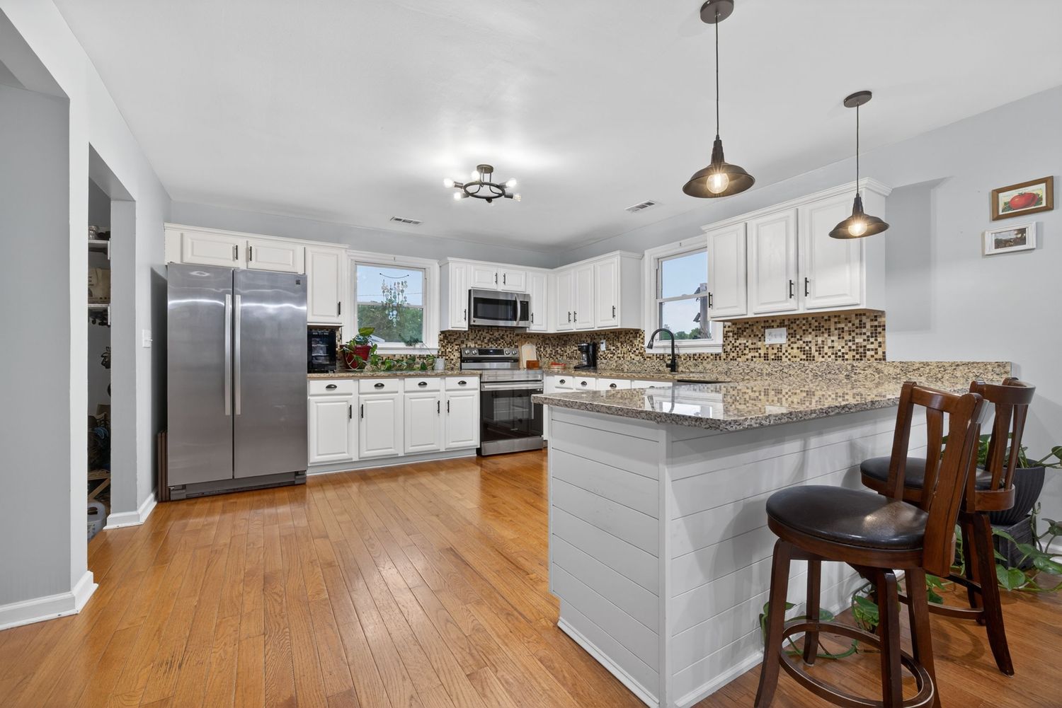 Modern kitchen with white cabinets, granite countertops, stainless steel appliances, pendant lights, and hardwood floors.