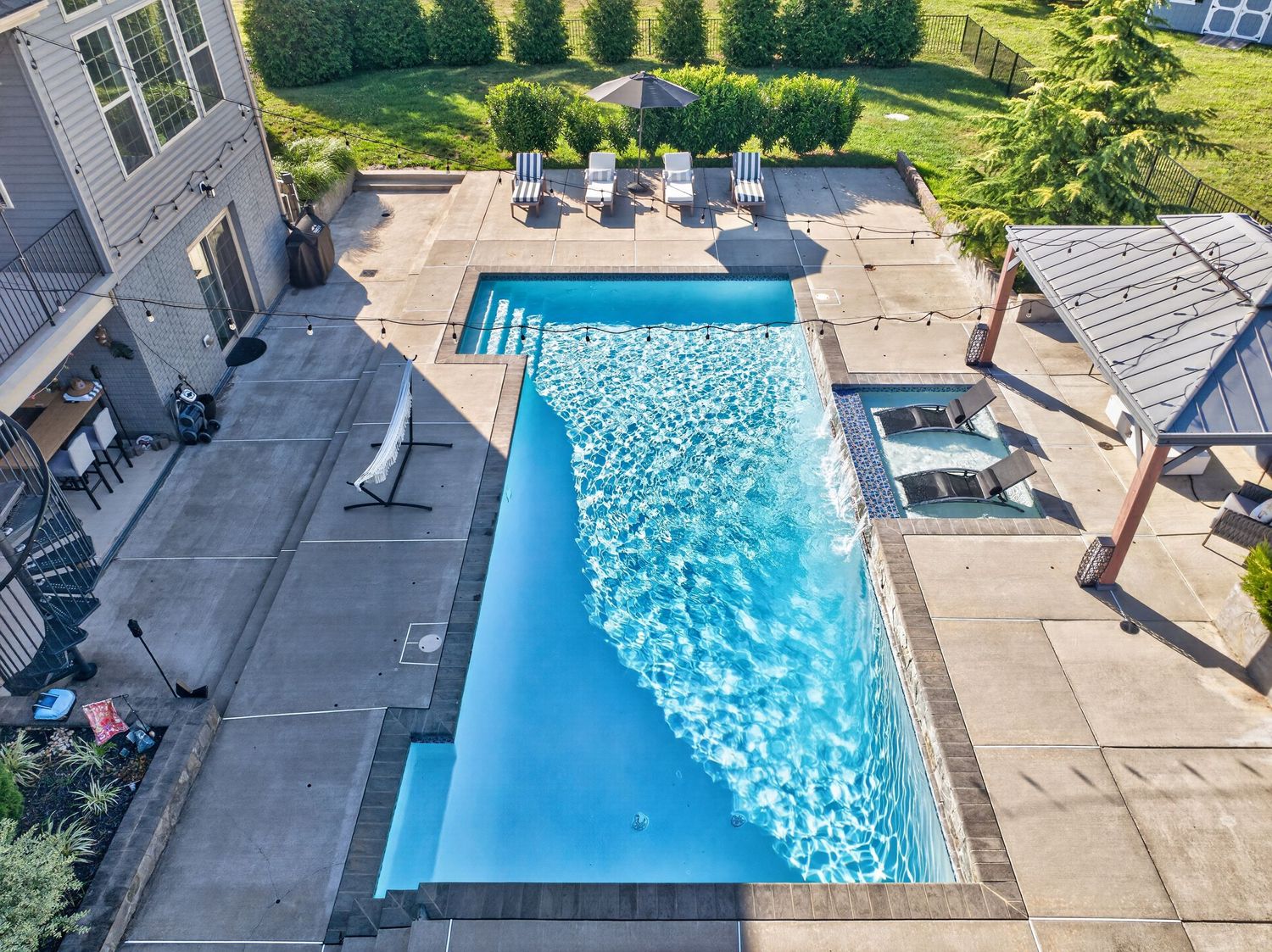 Aerial view of a rectangular backyard swimming pool with crystal blue water, surrounded by a patio with lounge chairs.