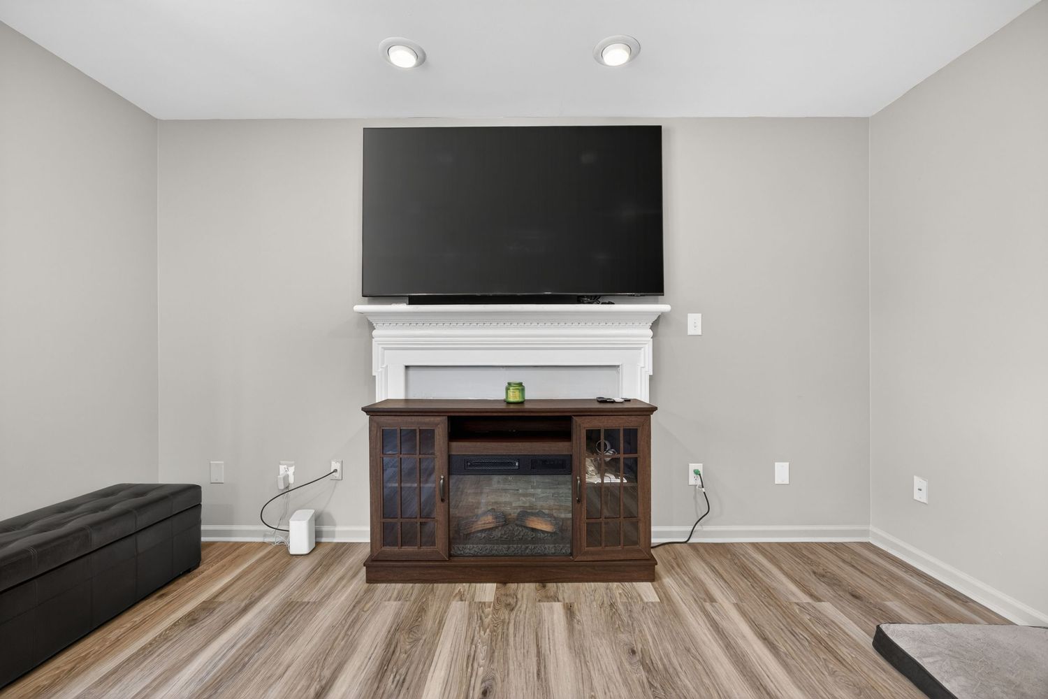 Living room with electric fireplace, dark wood mantel, wall-mounted TV, and light hardwood floors.