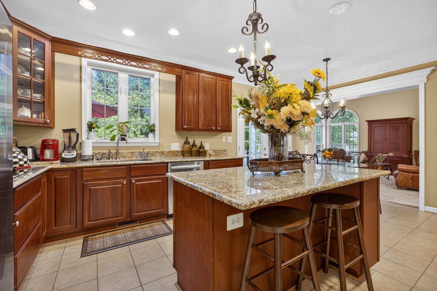 Elegant kitchen with cherry wood cabinets, granite island, bar stools, chandelier, and large windows with natural light.