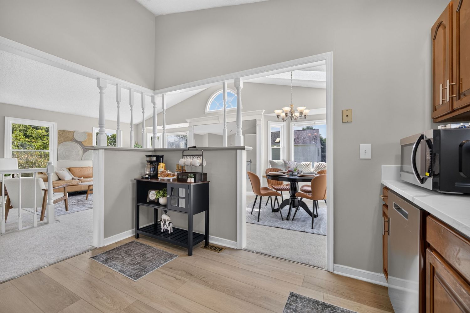 Bright open-concept home interior with hardwood floors, high ceilings, dining area, and chandelier visible through wide doorway.