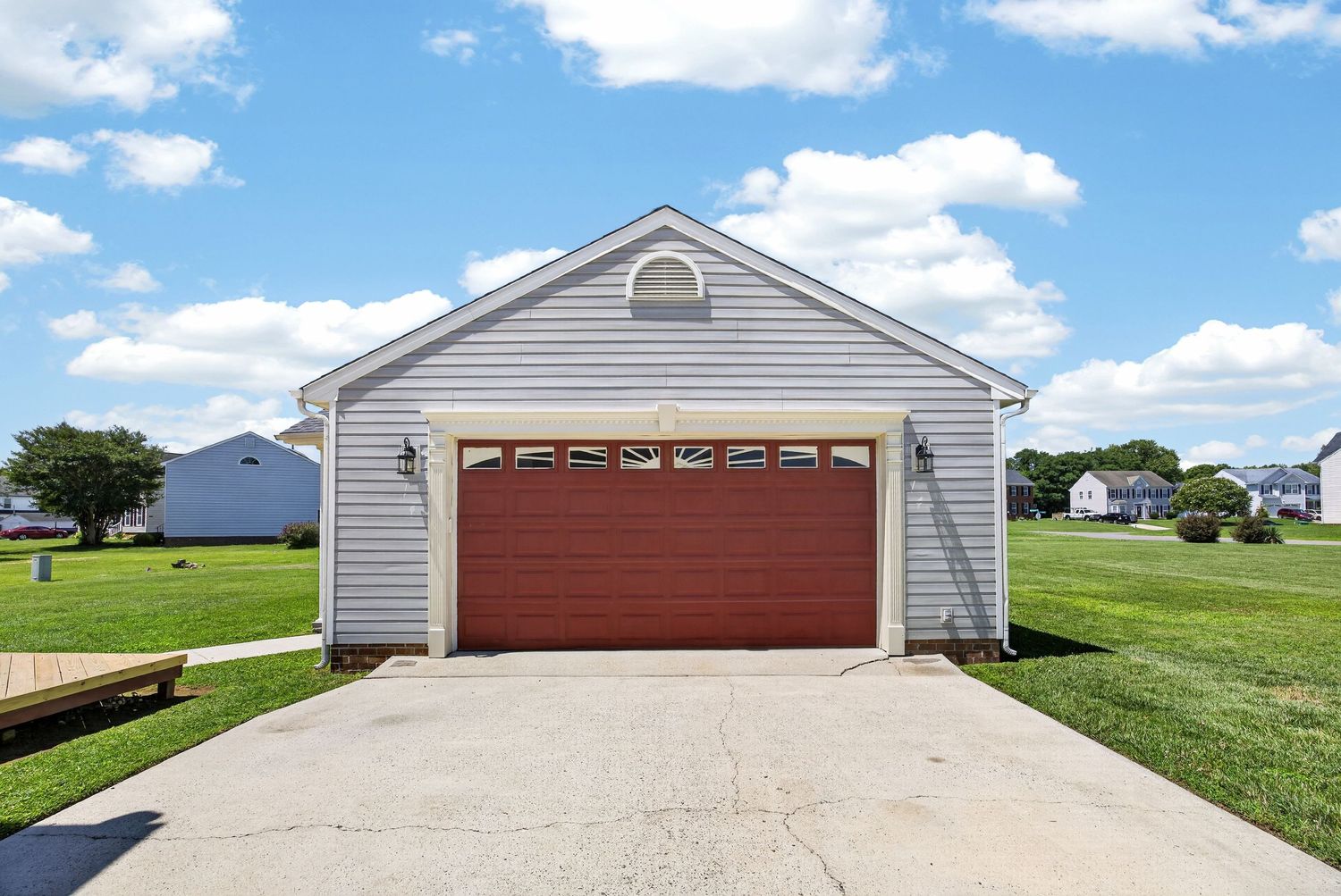 Detached two-car garage with red door, gray siding, and concrete driveway surrounded by lush green lawn.