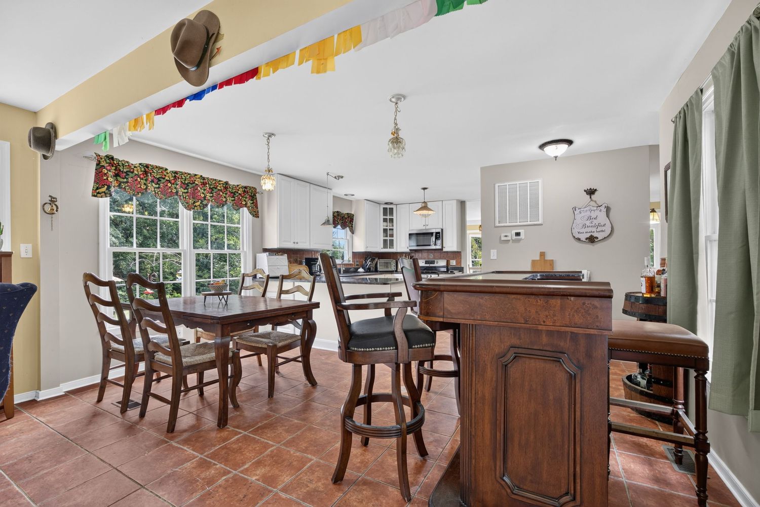 Spacious open-concept dining area with wooden bar, tile floors, and colorful ceiling decorations leading to a bright kitchen.