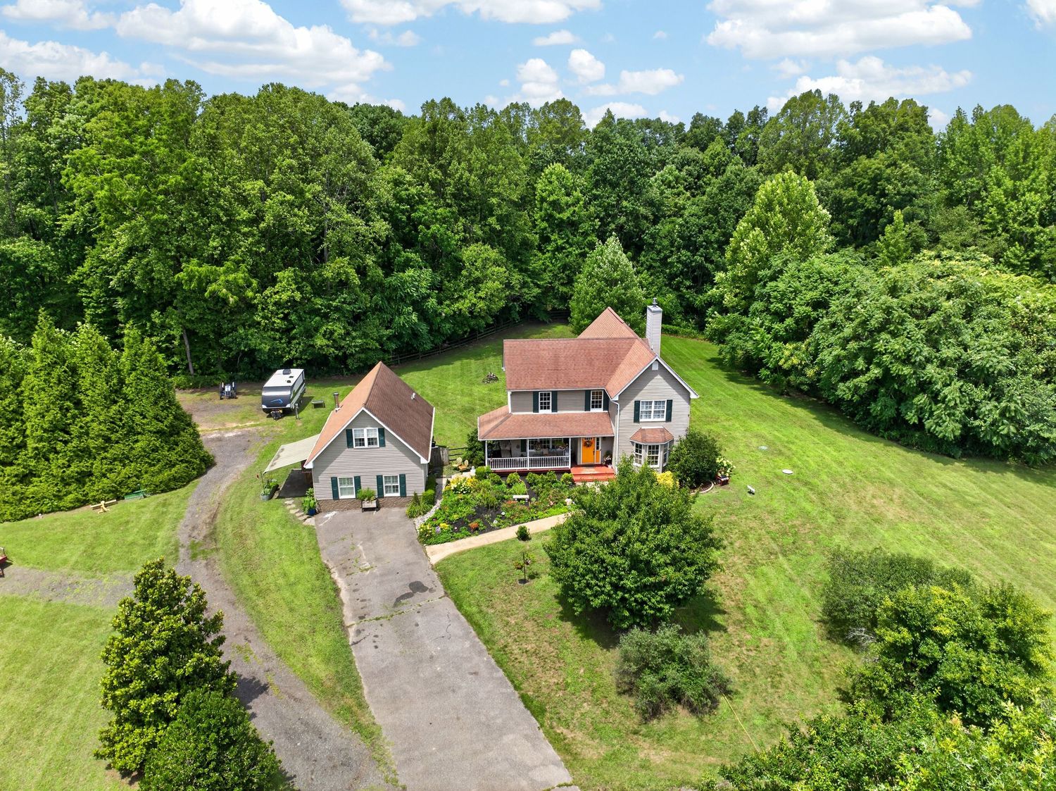 Aerial view of a two-story home with red roof surrounded by lush green trees and manicured lawn with long driveway.