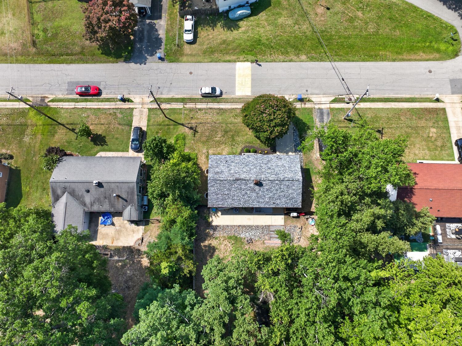 Aerial view of suburban homes with gray rooftops surrounded by lush green trees along a quiet residential street.