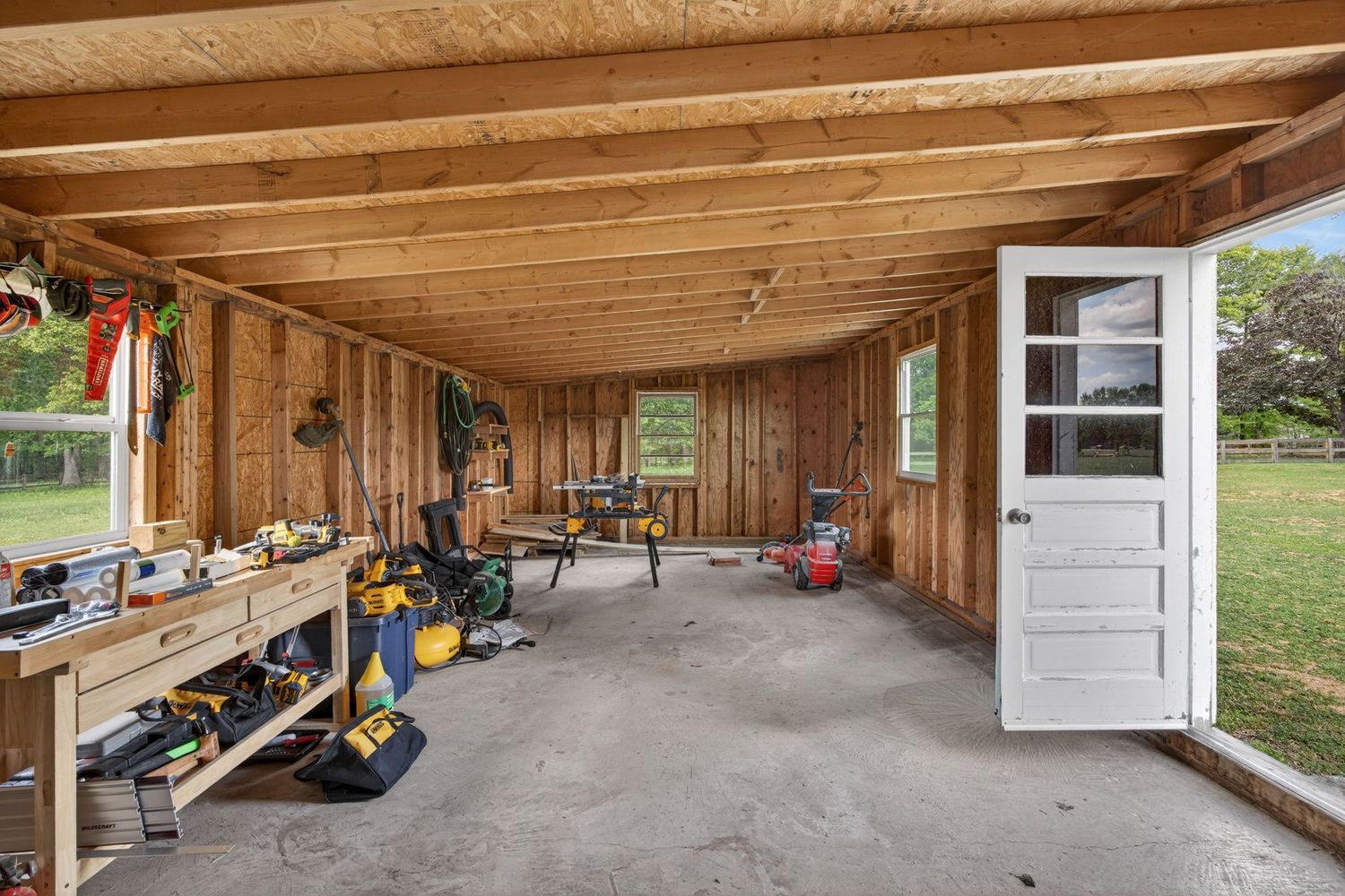 Rustic wooden workshop with workbench, tools, and open layout under exposed beam ceiling with natural light.