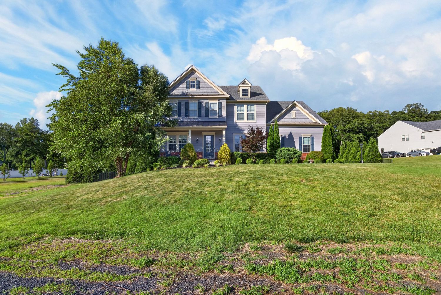 Large two-story craftsman home on a lush green hill surrounded by mature trees under a blue sky.