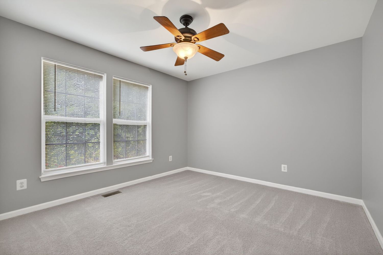 Empty bedroom with gray walls, ceiling fan, carpet flooring, and a double window with natural light.