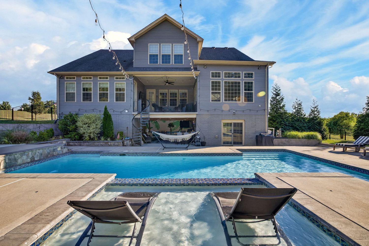 Luxury home backyard featuring a rectangular pool, lounge chairs, and a large two-story house with a covered patio.