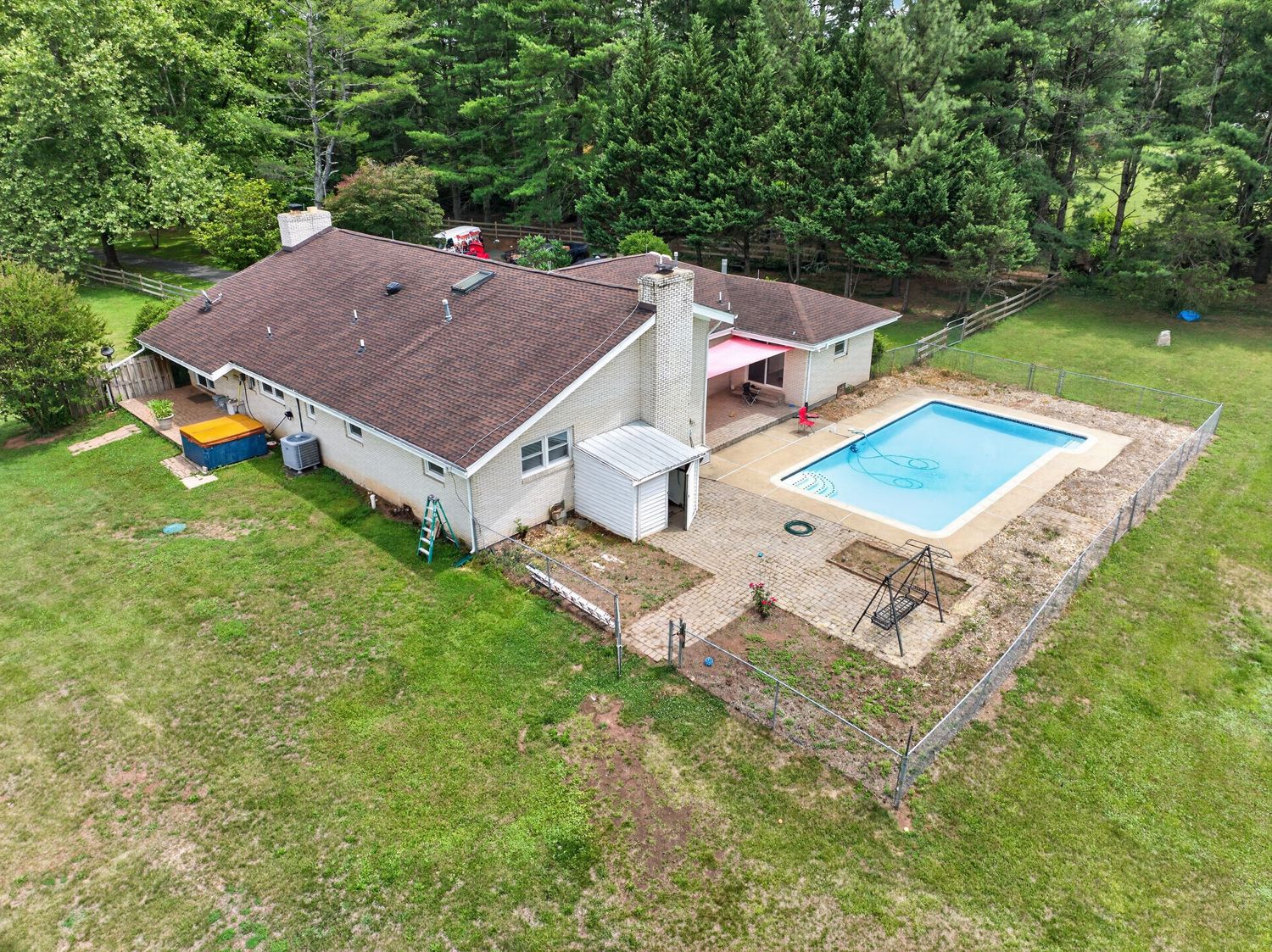 Aerial view of a residential home with a backyard swimming pool surrounded by lush green trees and manicured lawn.