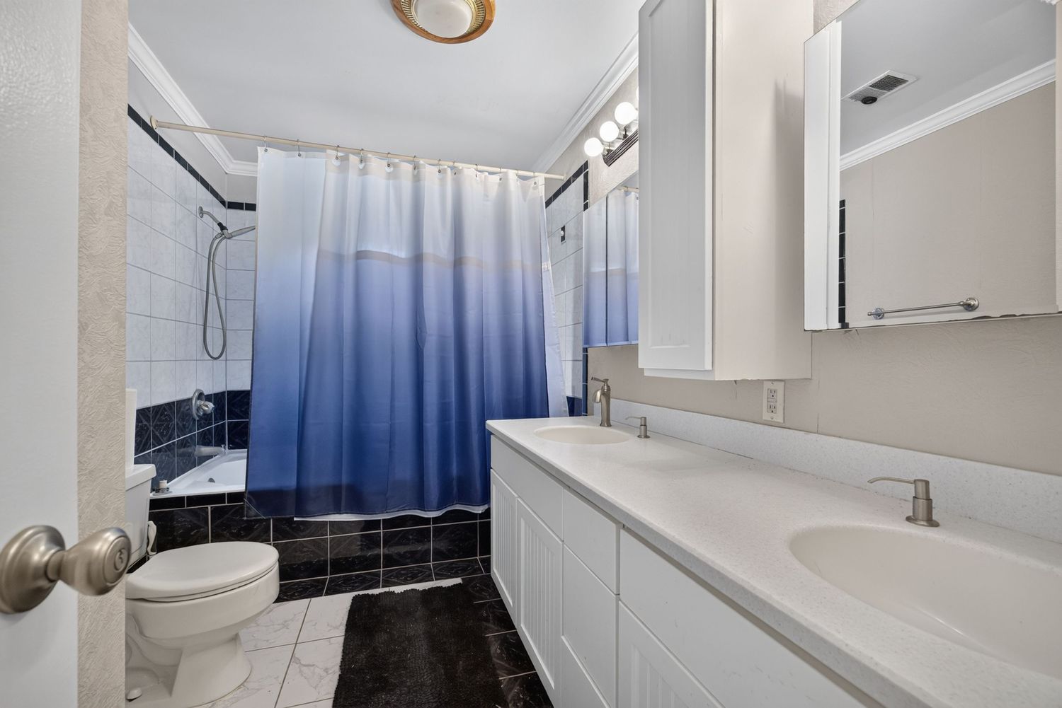 Modern bathroom with blue ombre shower curtain, white double vanity, toilet, and dark tile flooring.