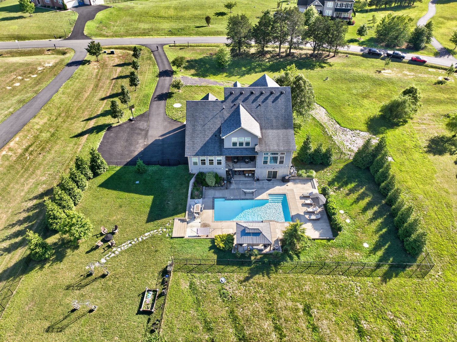 Aerial view of a large luxury home with a backyard swimming pool surrounded by lush green lawns and tree-lined driveway.