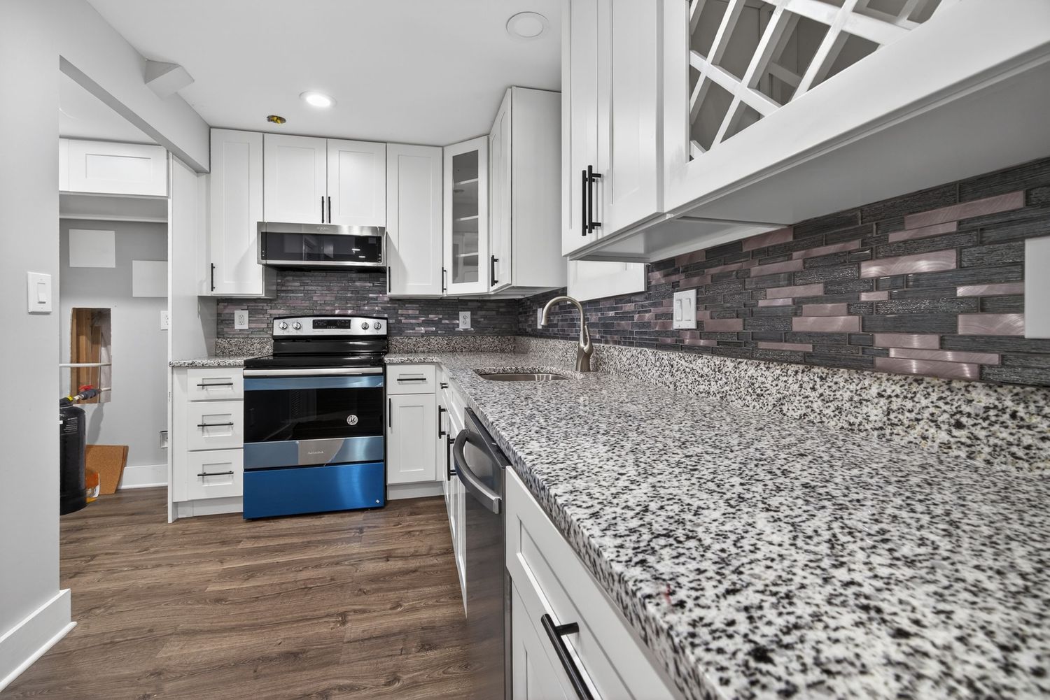 Modern kitchen with white cabinets, granite countertops, stainless steel appliances, and decorative tile backsplash.