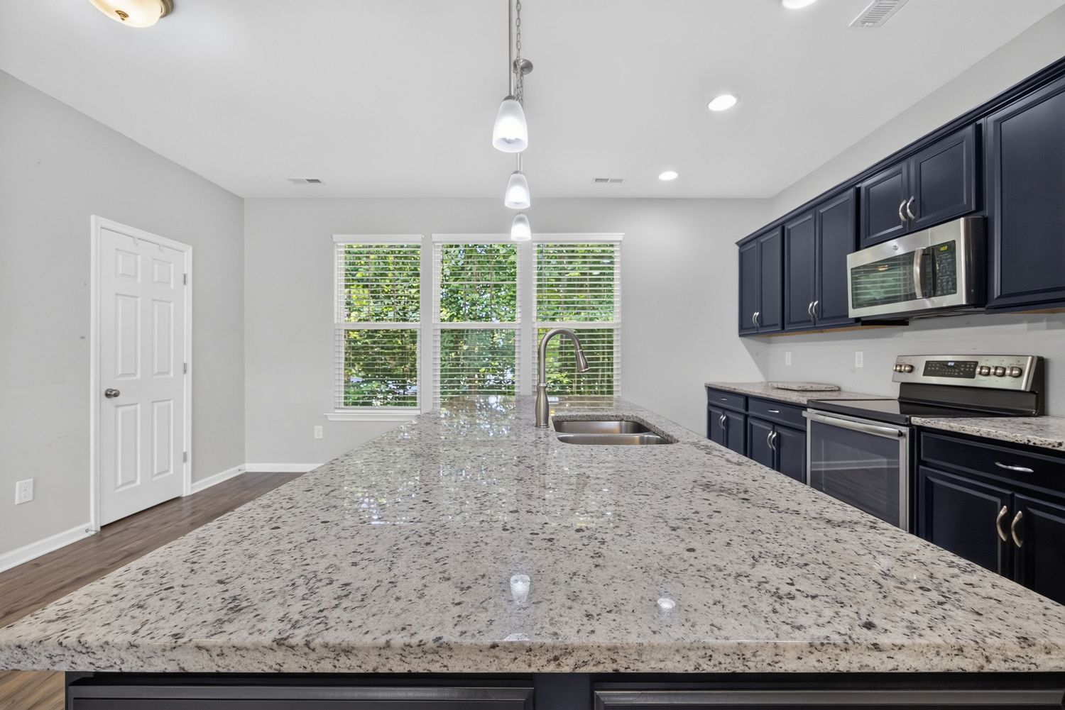 Modern kitchen with granite island, navy cabinets, stainless steel appliances, and pendant lighting over hardwood floors.