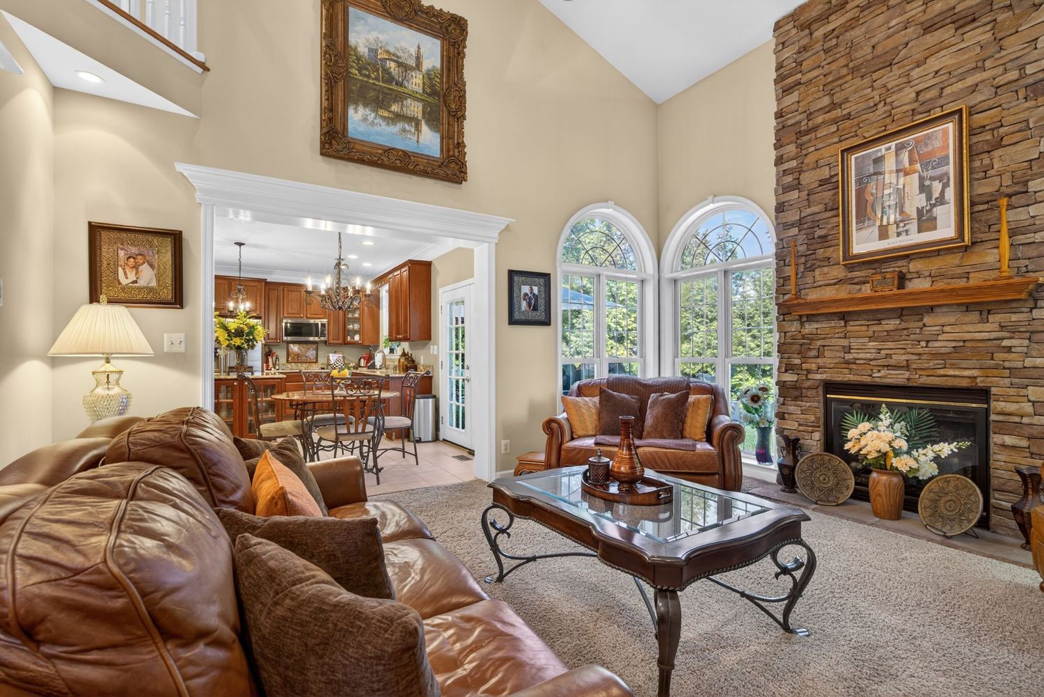 Elegant living room with leather sofas, stone fireplace, high ceilings, and arched windows overlooking lush greenery.
