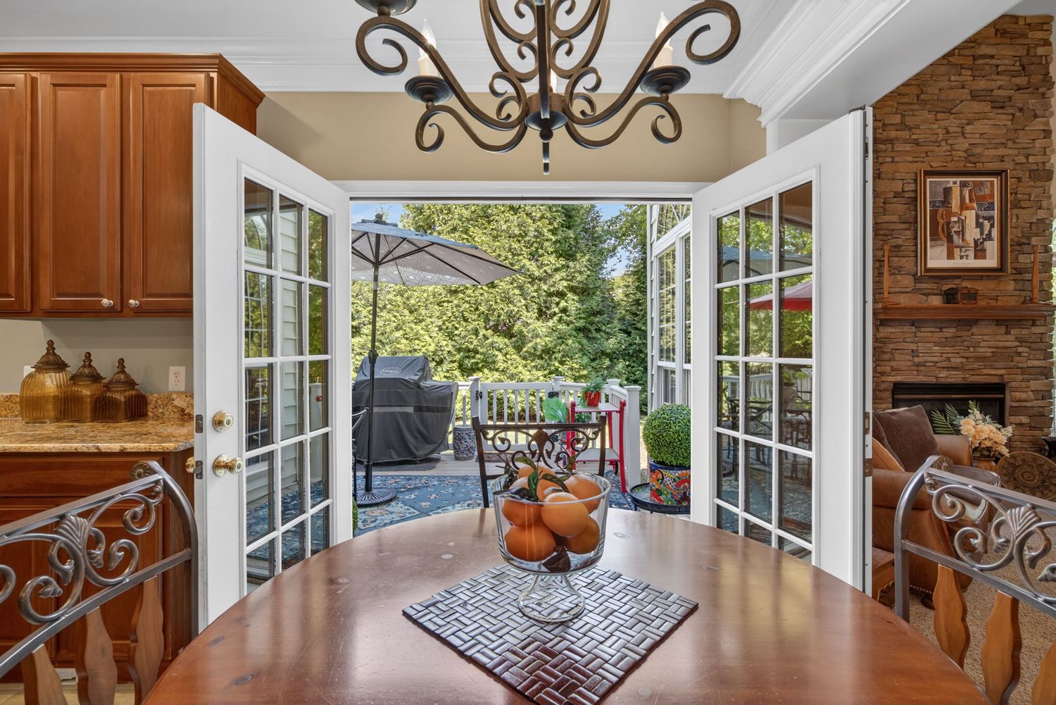Elegant dining room with French doors opening to a patio, hardwood floors, chandelier, and brick fireplace.