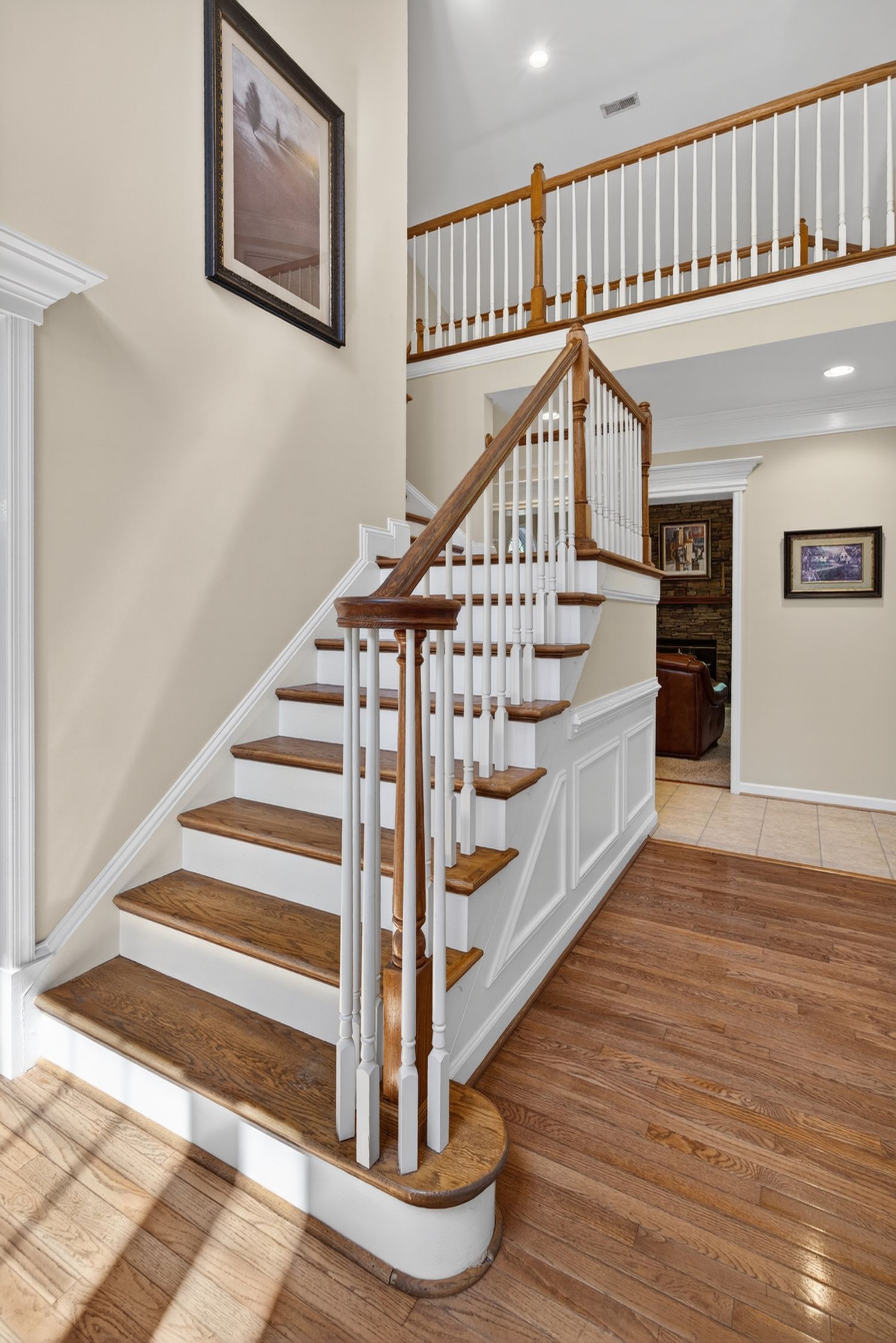 Elegant two-story foyer featuring hardwood stairs with white balusters, oak handrail, wainscoting, and an open second-floor balcony.