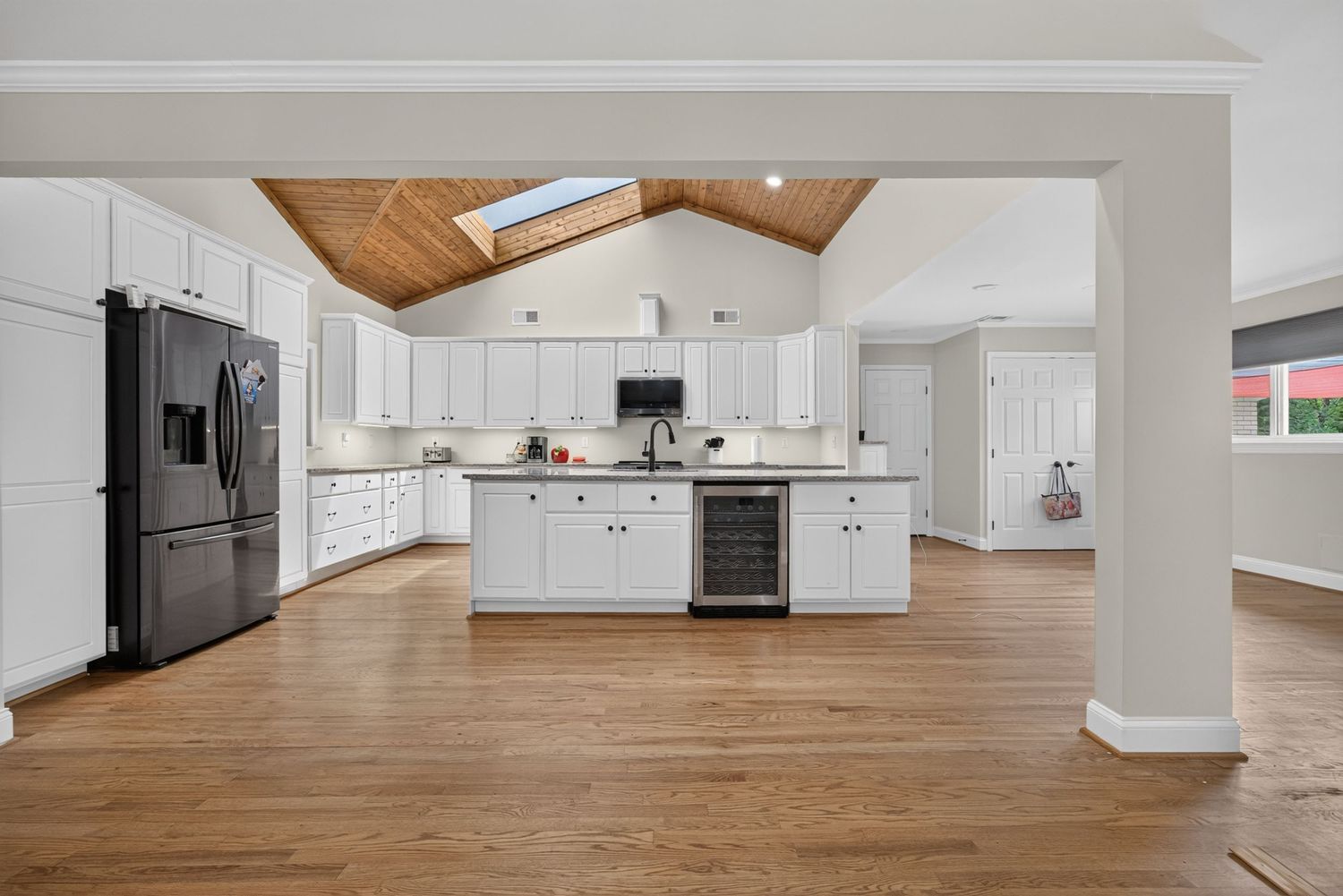 Spacious open-plan kitchen with white cabinets, black appliances, hardwood floors, and vaulted wood-paneled ceiling with skylight.