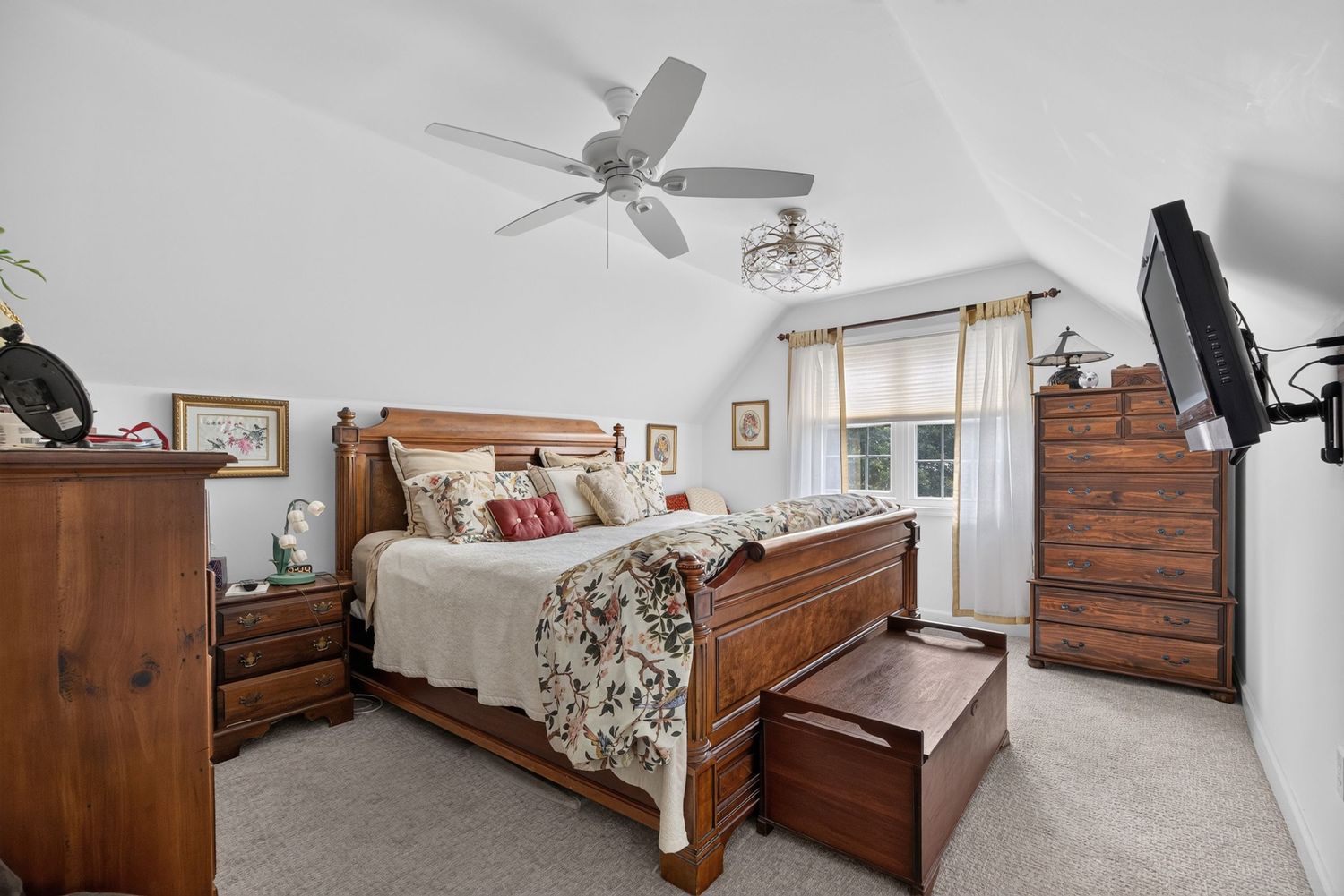 Cozy master bedroom with wooden sleigh bed, matching dresser, ceiling fan, and carpeted floors under vaulted ceiling.