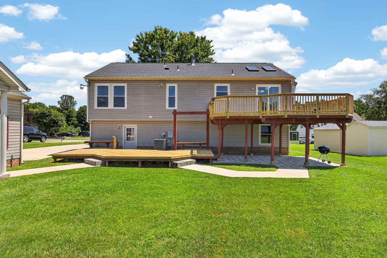 Two-story home with large wooden deck, patio area, and lush green lawn on a sunny day.
