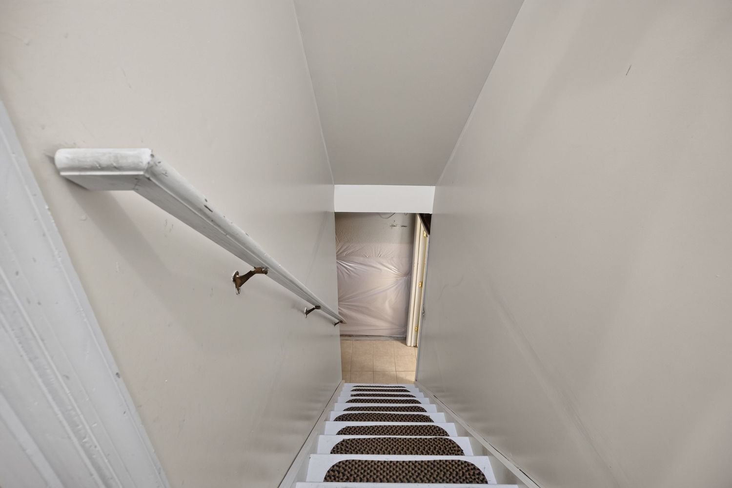Narrow staircase with white walls, wooden handrail, and dark non-slip stair treads leading to a doorway.