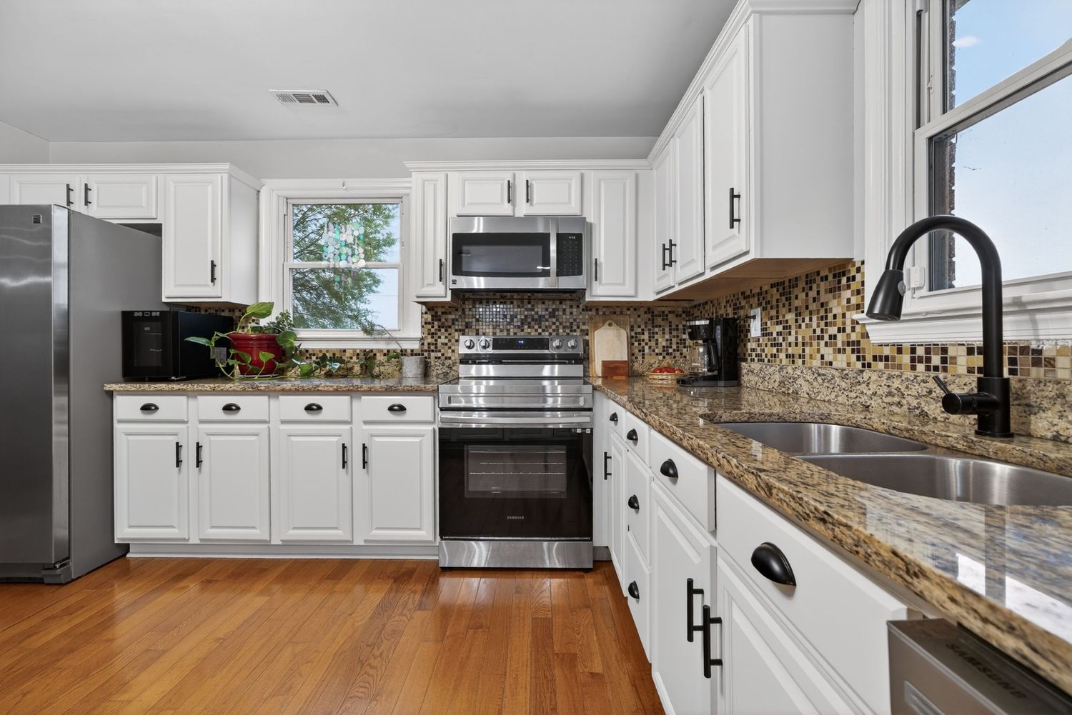 Modern kitchen with white cabinets, granite countertops, stainless steel appliances, mosaic backsplash, and hardwood floors.