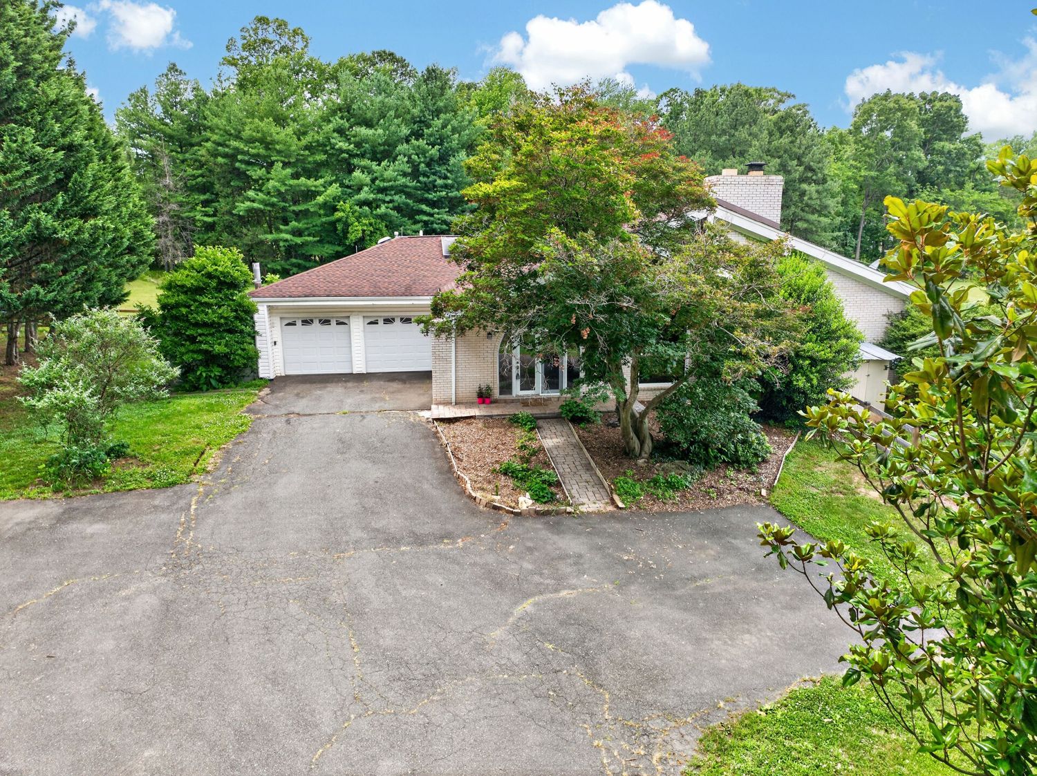 Aerial view of a residential home with a two-car garage, circular driveway, and lush green trees surrounding the property.