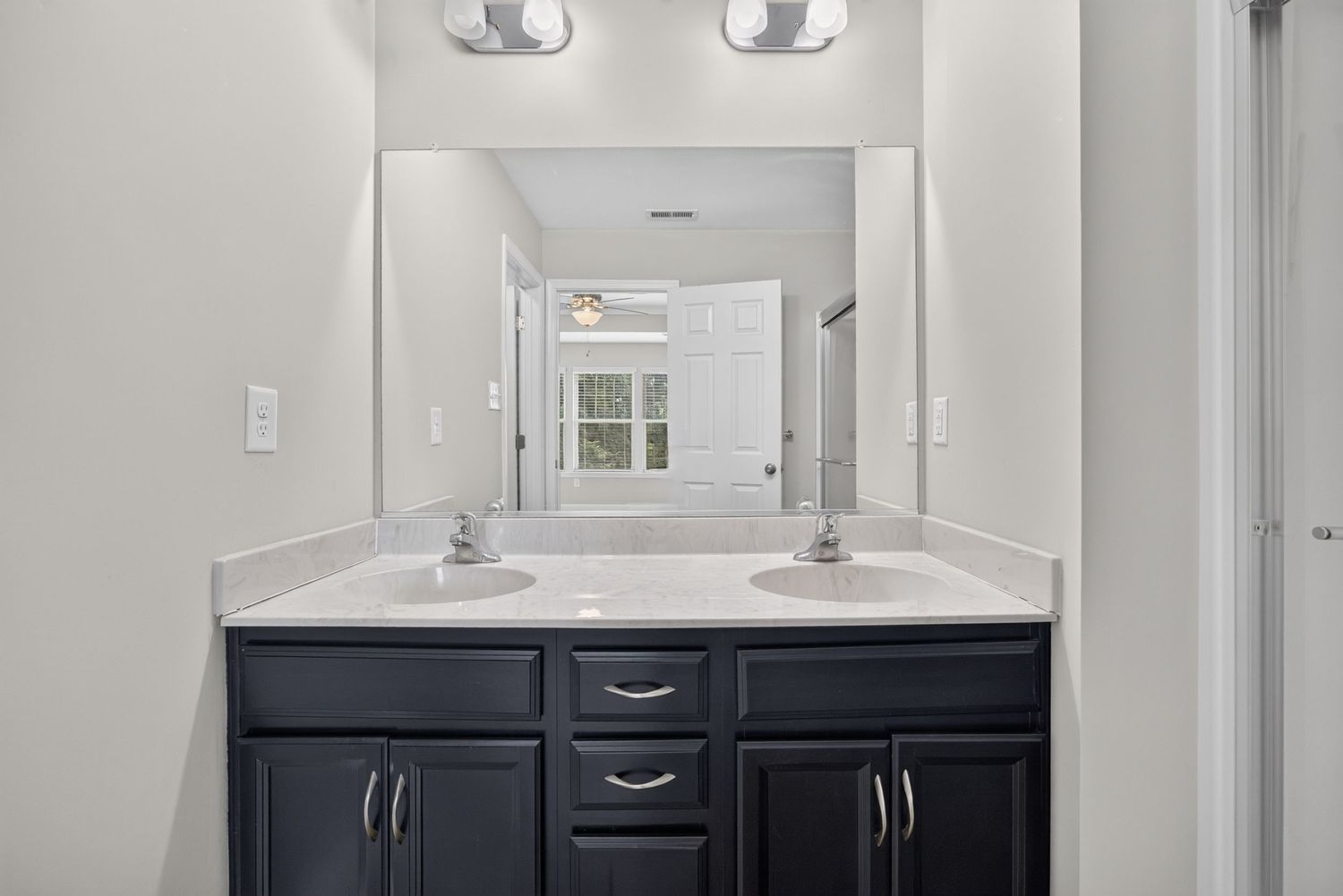 Modern bathroom with double sink vanity featuring dark navy cabinets, white countertops, and large mirror above.