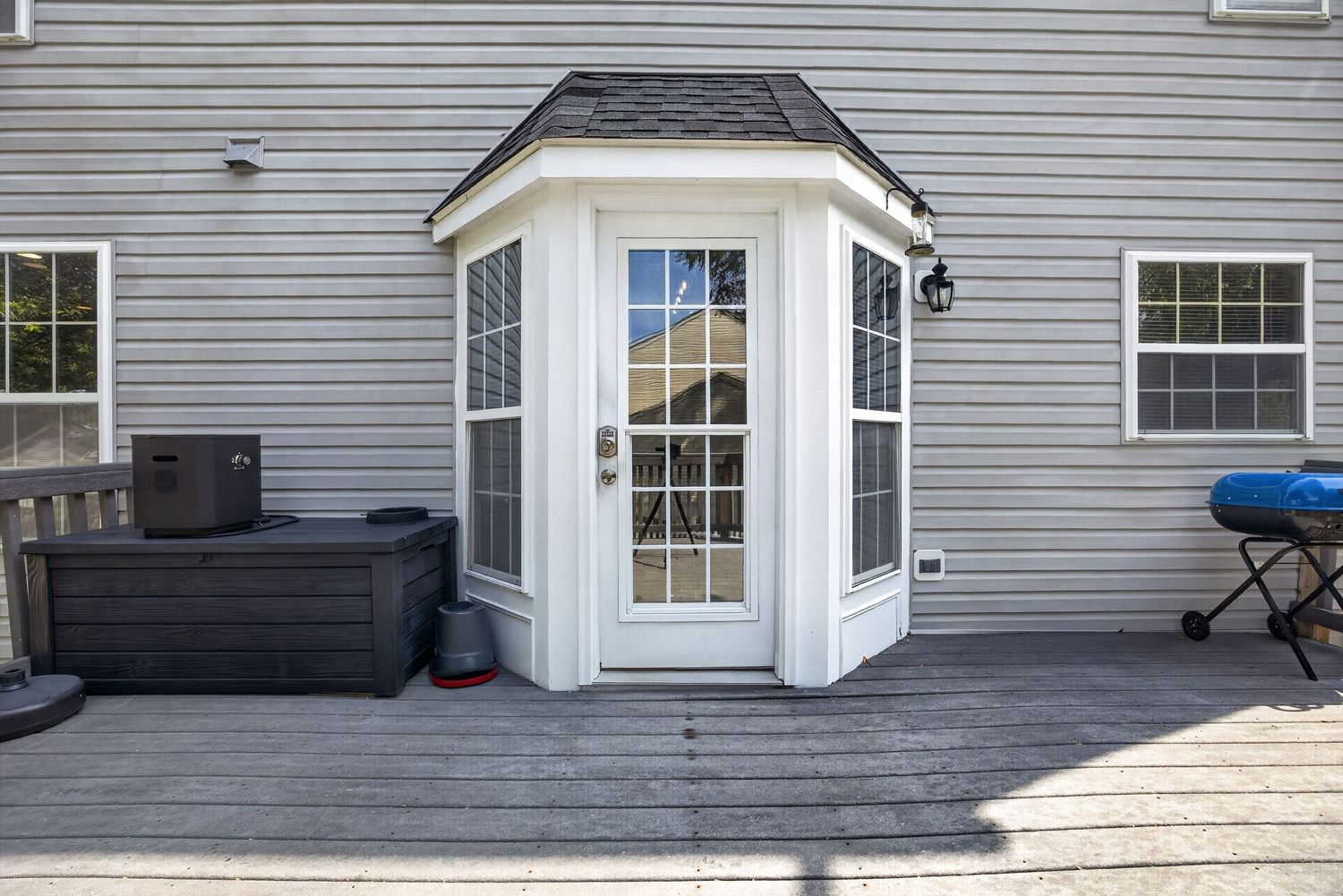 Gray house exterior featuring a white bay door entry with decorative windows on a wooden deck with hot tub.